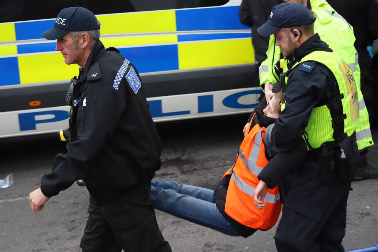 Policjanci niosą dziewczynę w pomarańczowej kamizelce.