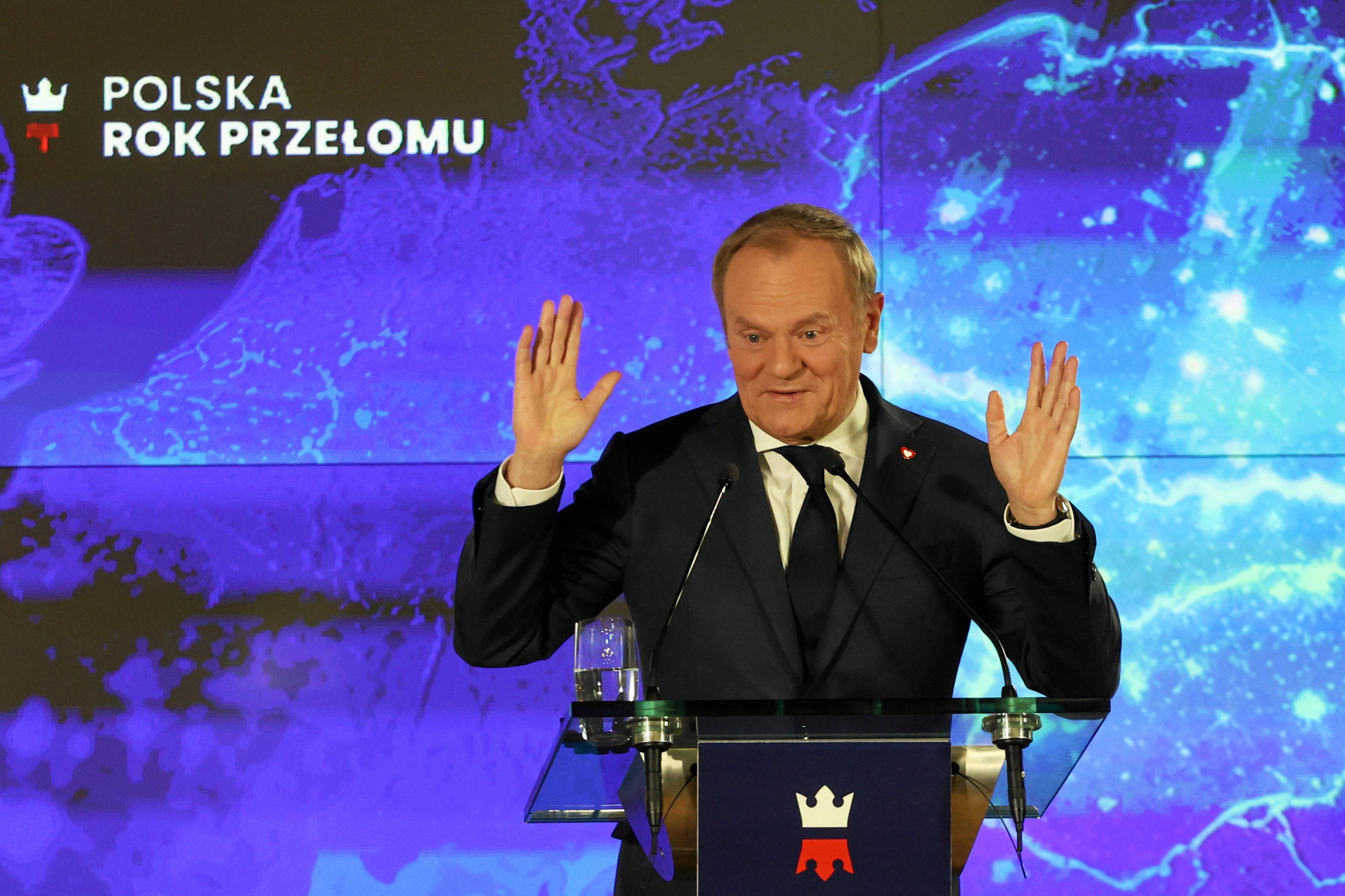 Donald Tusk podczas konferencji prasowej w siedzibie GPW gestykuluje rękami na tle napisu "Polska. Rok przełomu".