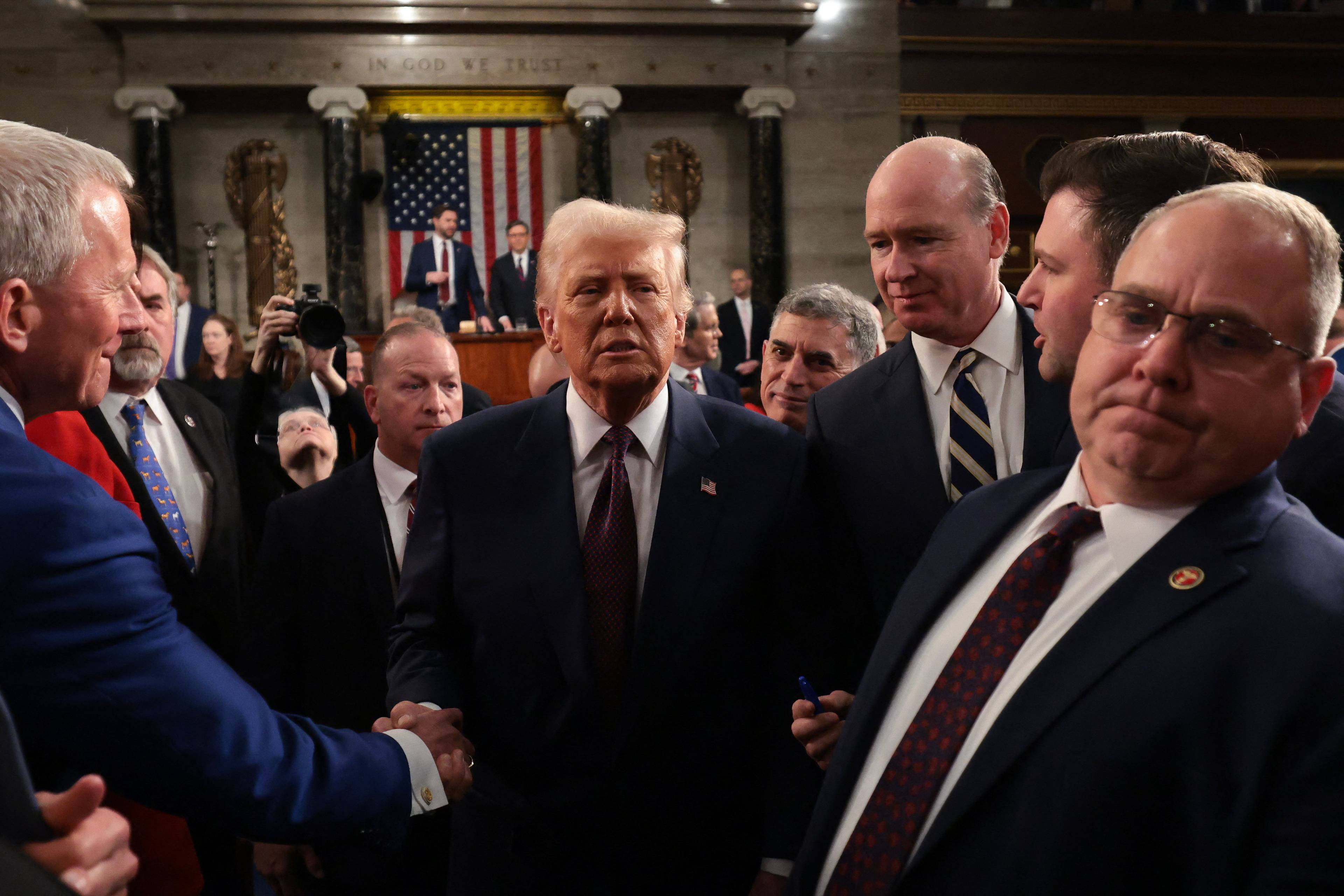 Donald Trump po przemówieniu w Kongresie ściska ręce słuchaczon. W tle mównica i flaga amerykańska