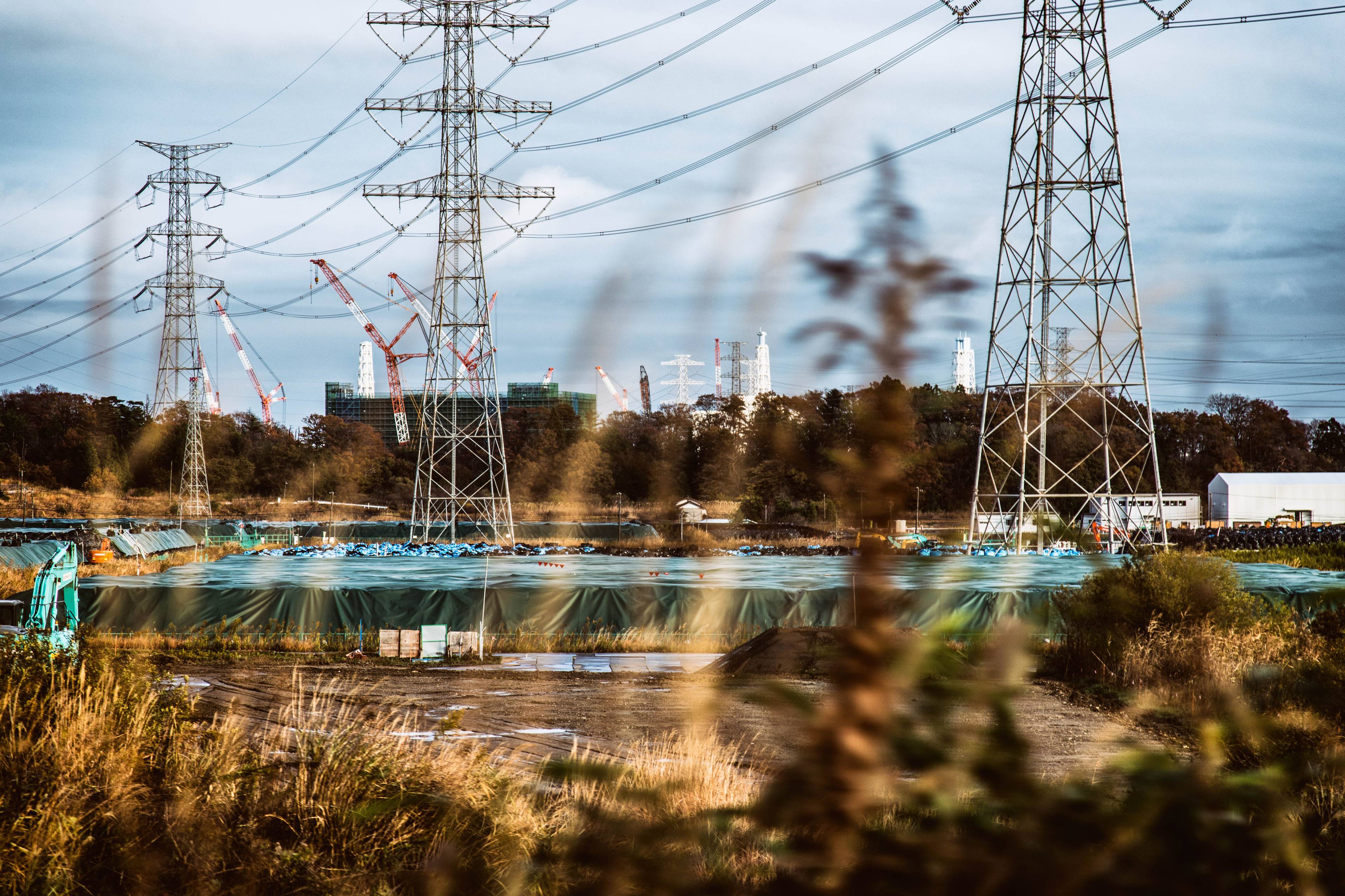 Widok na pryzmę ziemi przykrytą brezentem i słupy sieci elektrycznej wysokiego napięcia.