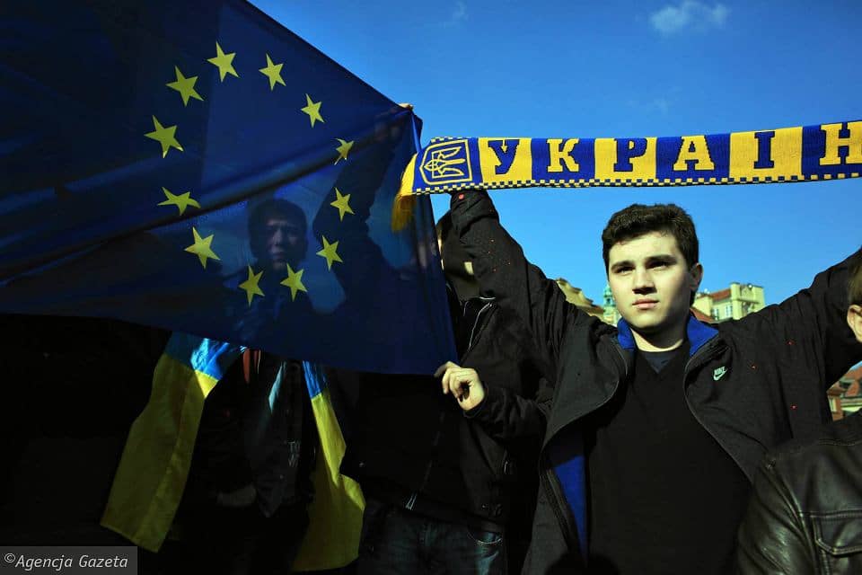 Mężczyzna z banerem z napisem Ukraina, w tle niebieska flaga UE ze złotymi gwiazdkami