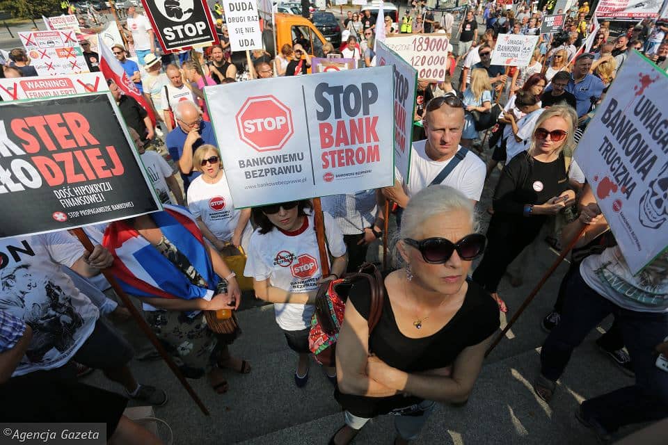 Demonstracja frankowiczów pod Belwederem, kobieta trzyma w ręku plakat z napisem Stop banksterom