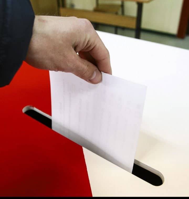 Dłoń wrzuca kartkę do urny wyborczej