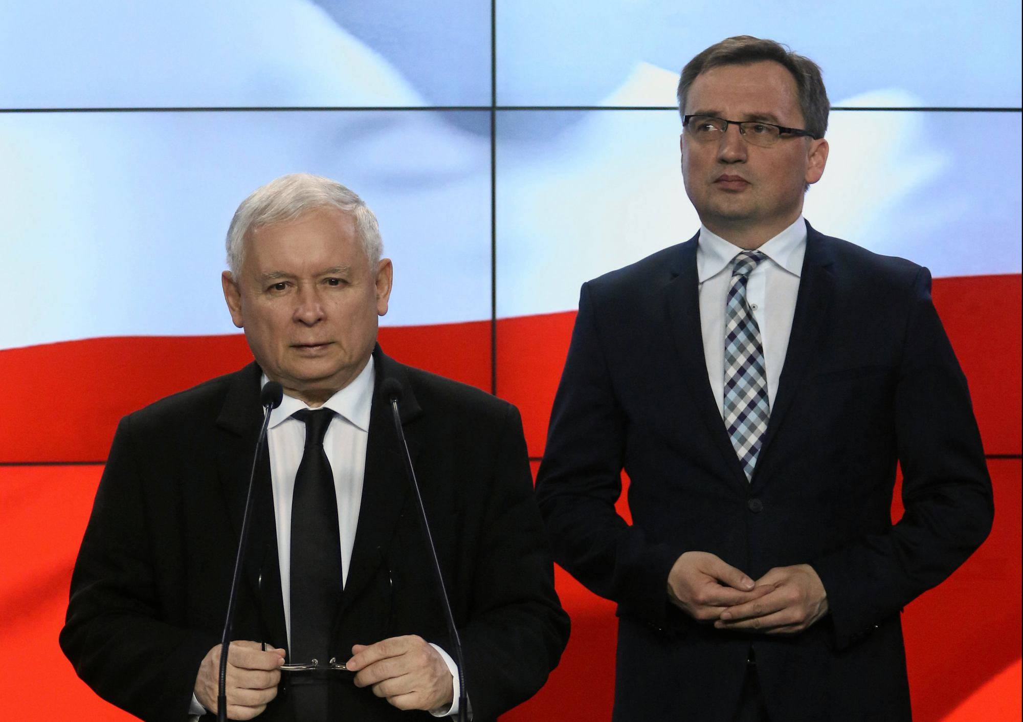Stoją Jarosław Kaczyński stoi przy mównicy, z tyłu Zbigniew Ziobro