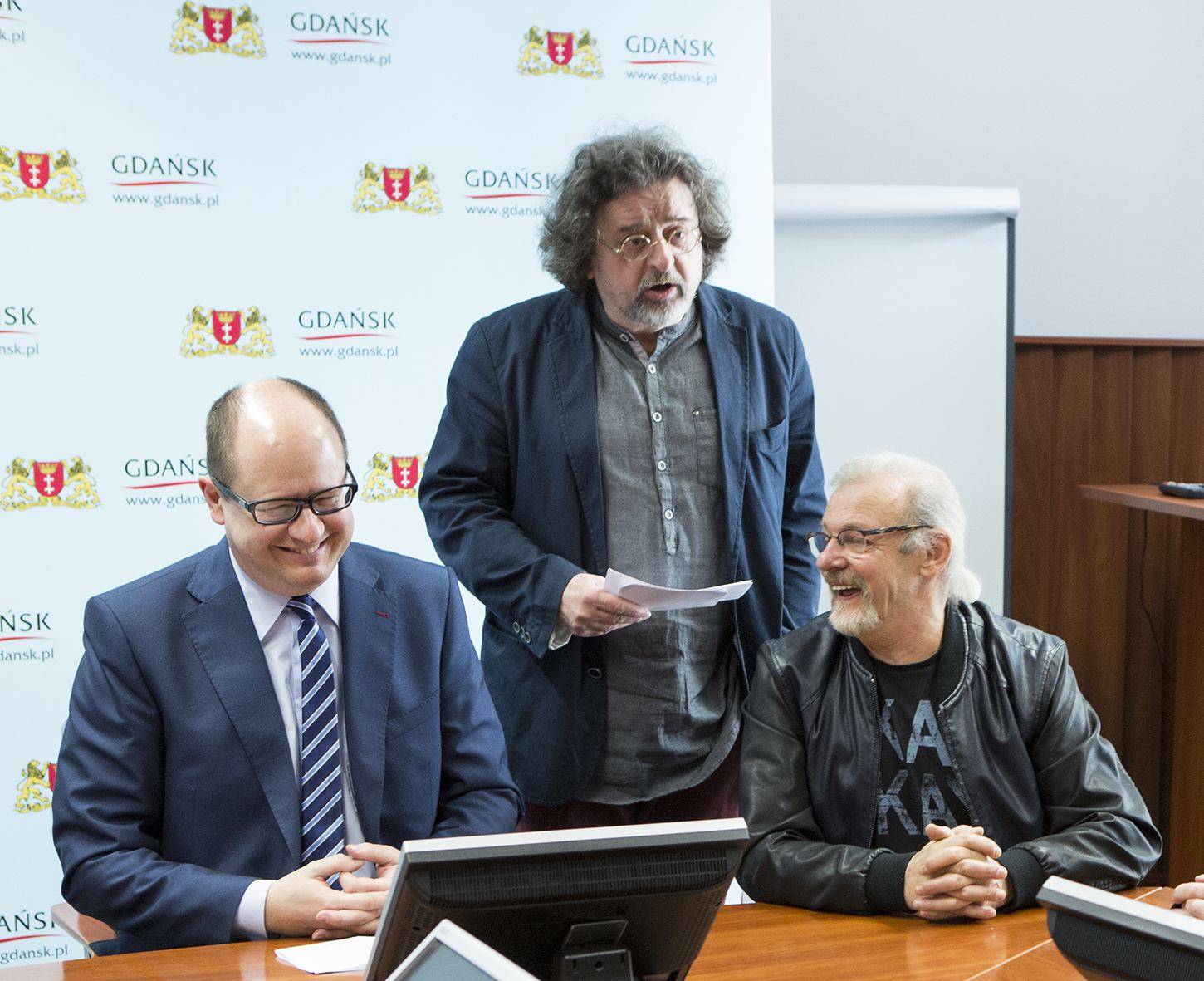 Paweł Adamowicz siedxzi uśmiechnięty, obok stoi jego ówczesny rzecznik Antoni Pawlak