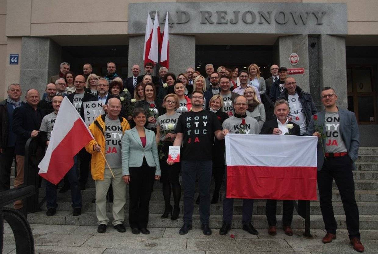 Uśmiechnięci sędziwoie stoją przed wejsćiem do Sądu Rejonowego w Olsztynie w koszulkach z napisem Konstytucja