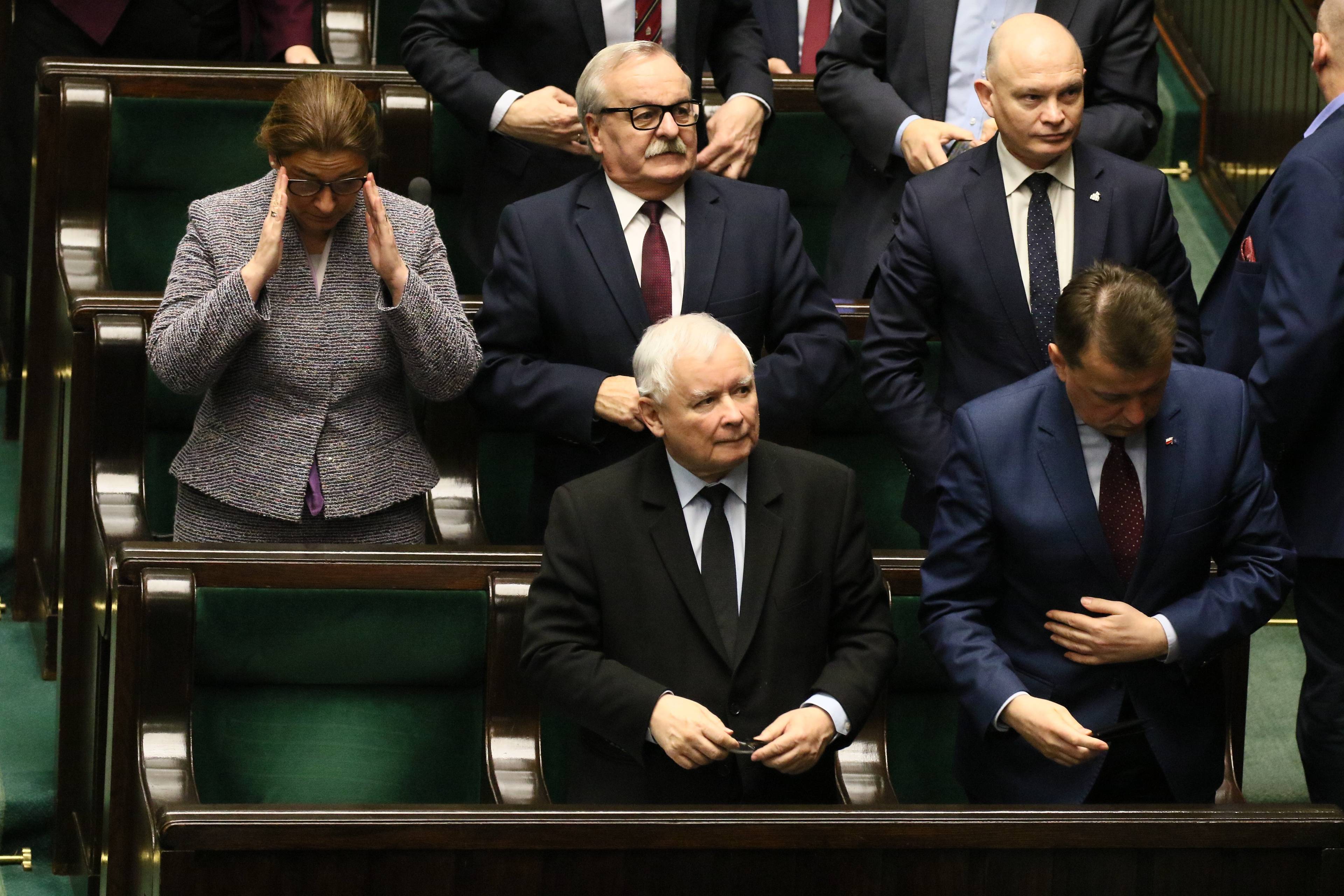 Jarosłąw Kaczyński stoi na swoim miejscu poselskim w Sejmie, patrzy w góre na wynik głosowania. Wokół niego Beata Mazurek i Mariusz Błaszczak