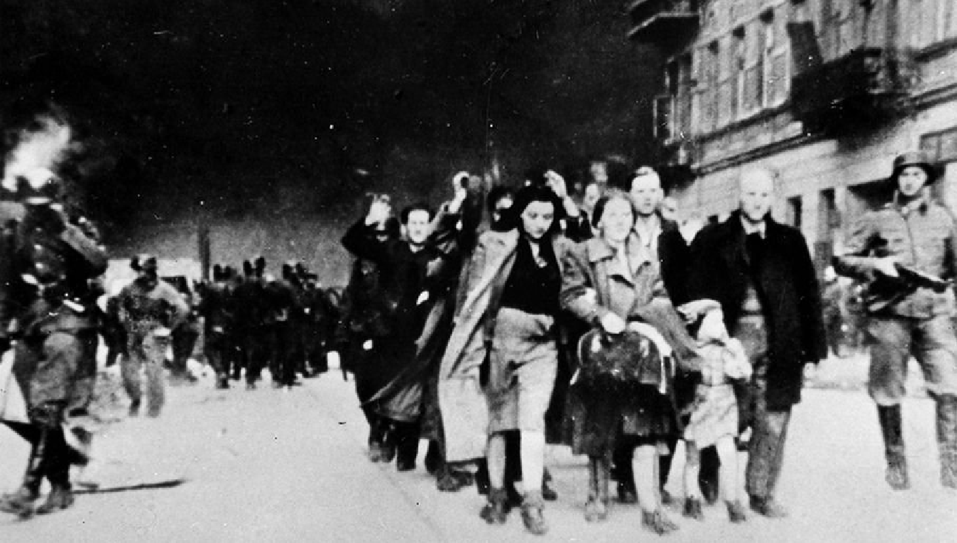 Likiwdacja getta warszawskiego, idzie tłum ludzi z podniesionymi rękami w otoczeniu uzbrojonych Niemców, w tle dymy palącego się getta w Warszawie