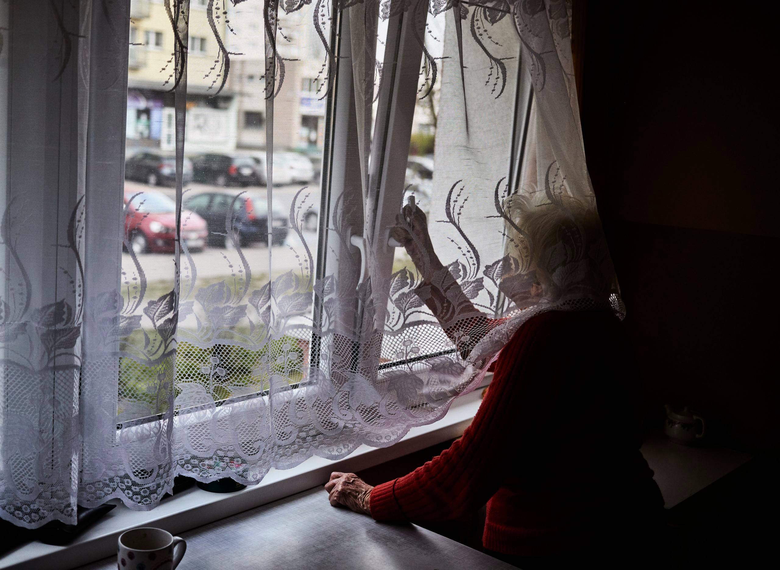 Starsza kobieta wygląda na ulicę przez zakratowane okno