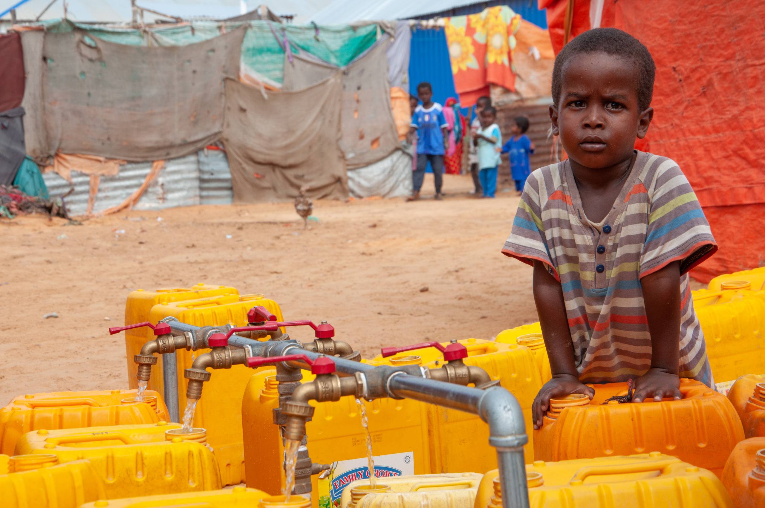 Somalia, mały chłopiec przy baniakach na wodę w obozie dla uchodźców