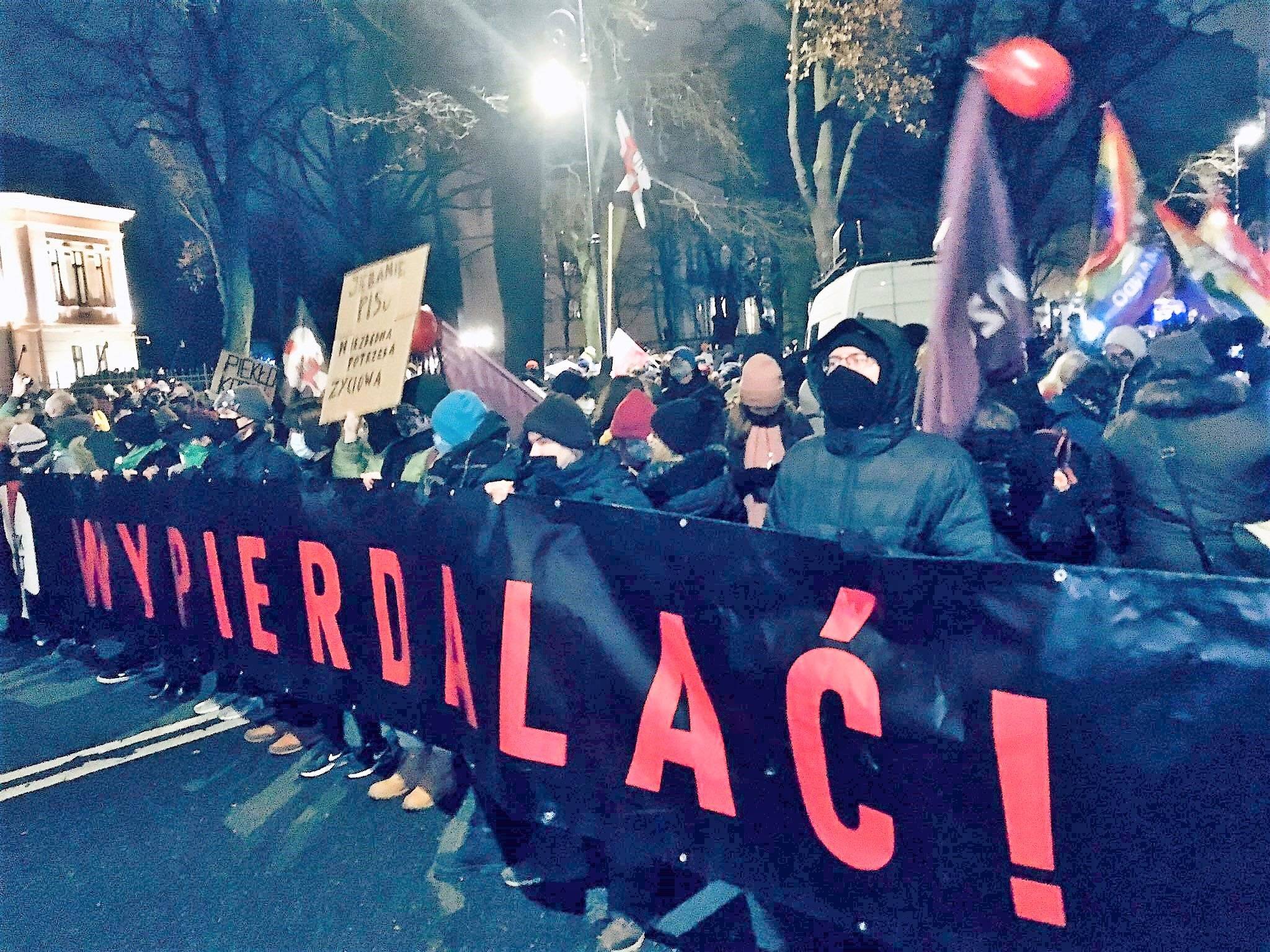 Protest Ogólnopolskiego strajku Kobiet pod Trybunałem Konstytucyjnym, ludzie trzymają wielki baner z czerwonym napisem Wypierdalać!