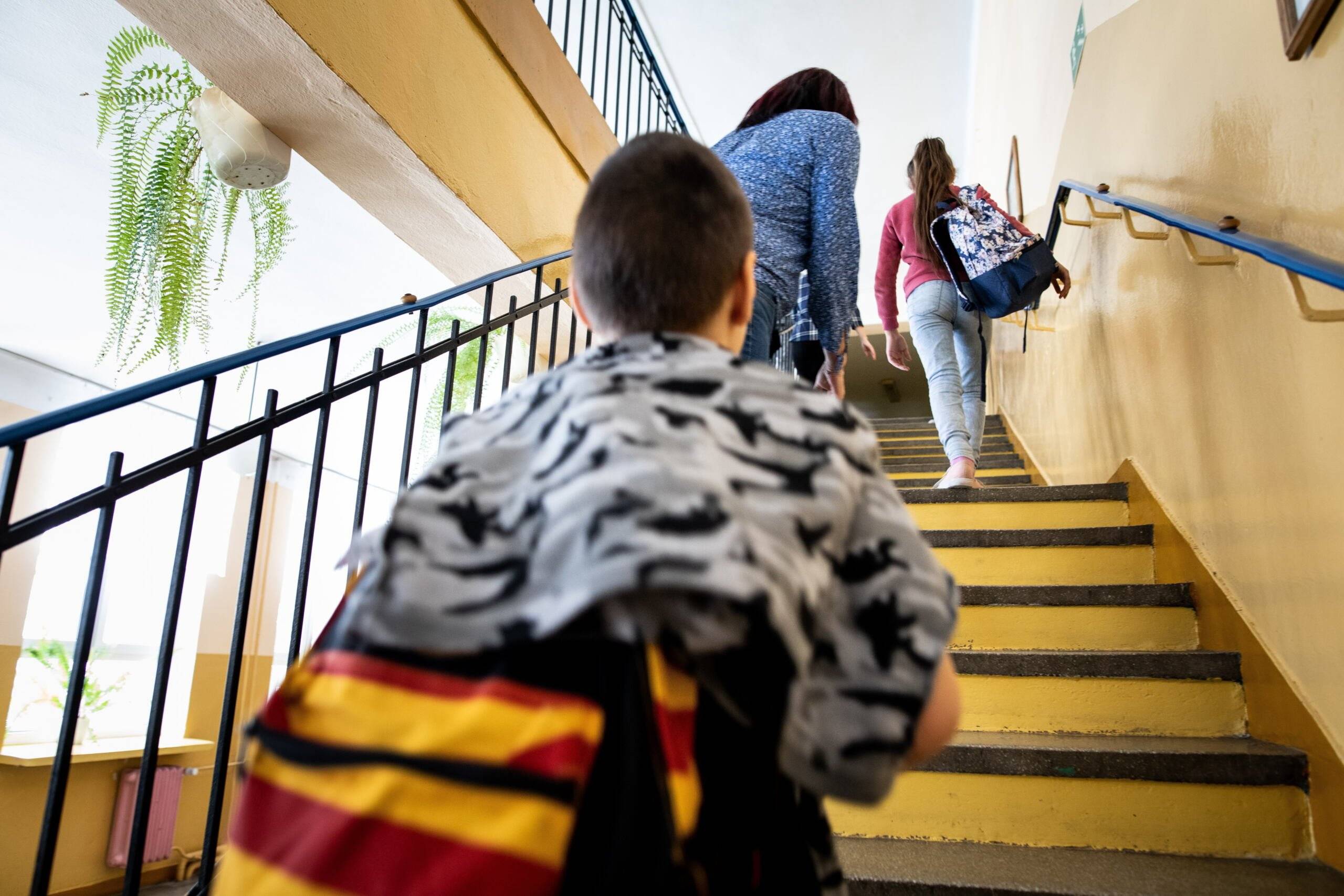 Szkoła w Bezwoli ma być zlikwidowana. Na zdjęciu chłopczyk wczhodzi po schodach, przed nim kobieta z zasłoniętą głową prowadzi córkę