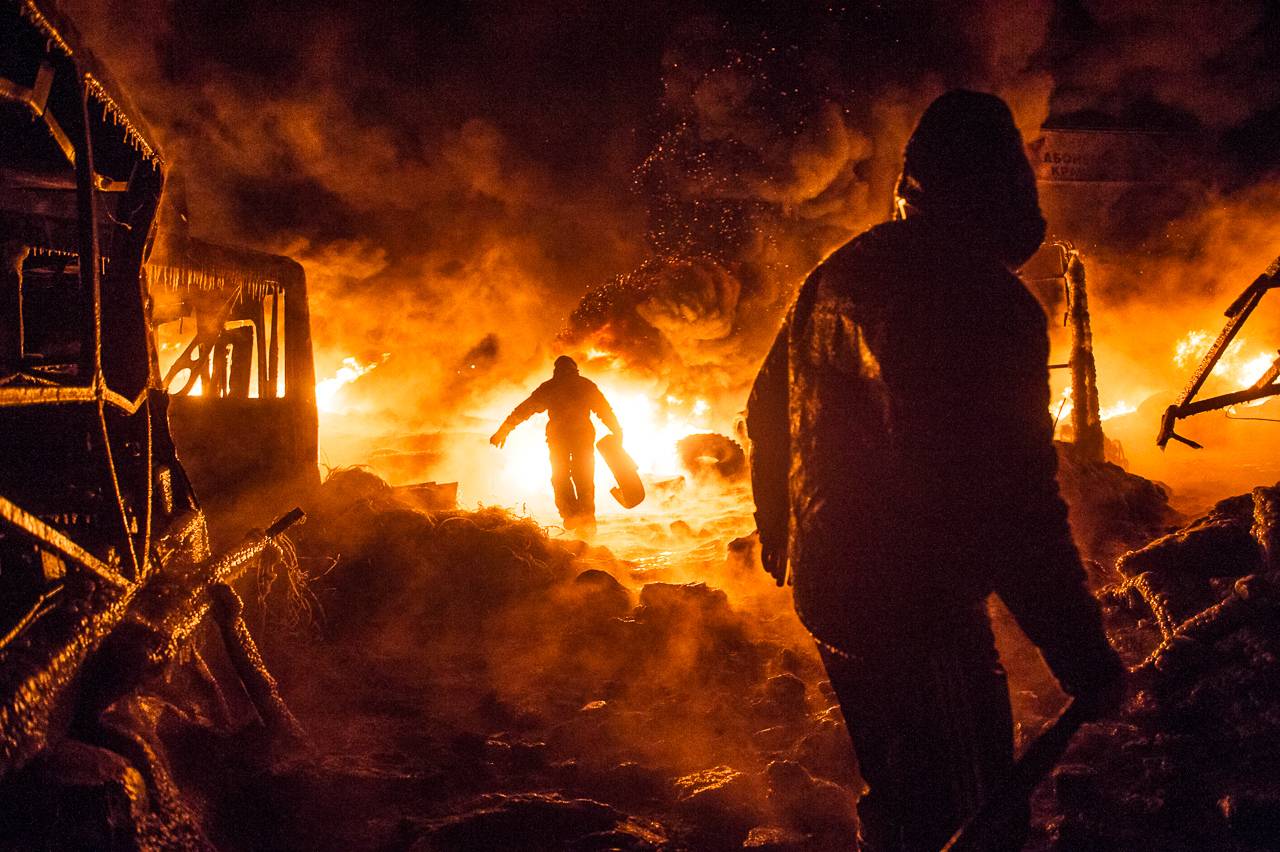 UKRAINE, Kiev : Ukrainian anti-government protesters walk past burning tyres during clashes with riot police in central Kiev early on January 25, 2014. Protesters and Ukrainian police were locked in a tense standoff in Kiev after a night of sporadic clashes that erupted despite a truce and offer of concessions by President Viktor Yanukovych. AFP PHOTO / VOLODYMYR SHUVAYEV