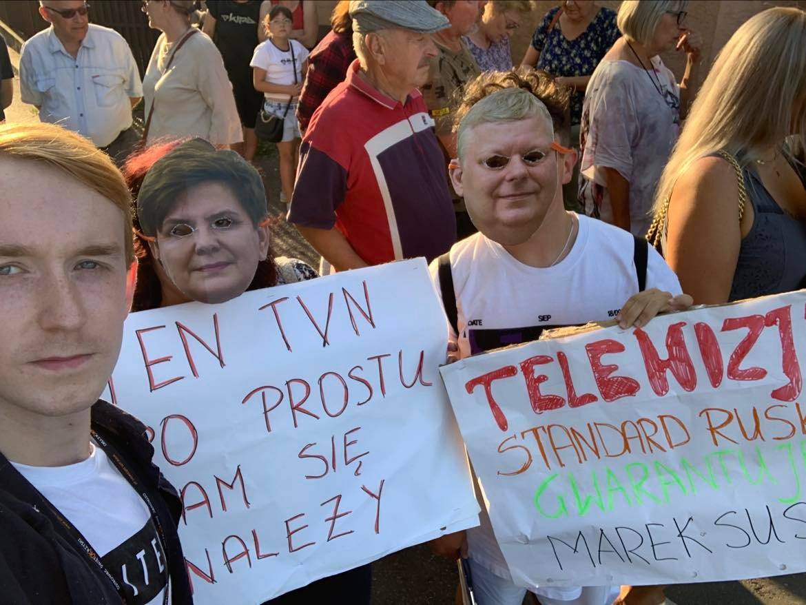 Ludzie z maskami twarzy Beaty Szydło i Marka Suskiego trzymają transparent "Ten TVN nam się po prostu nalezy"