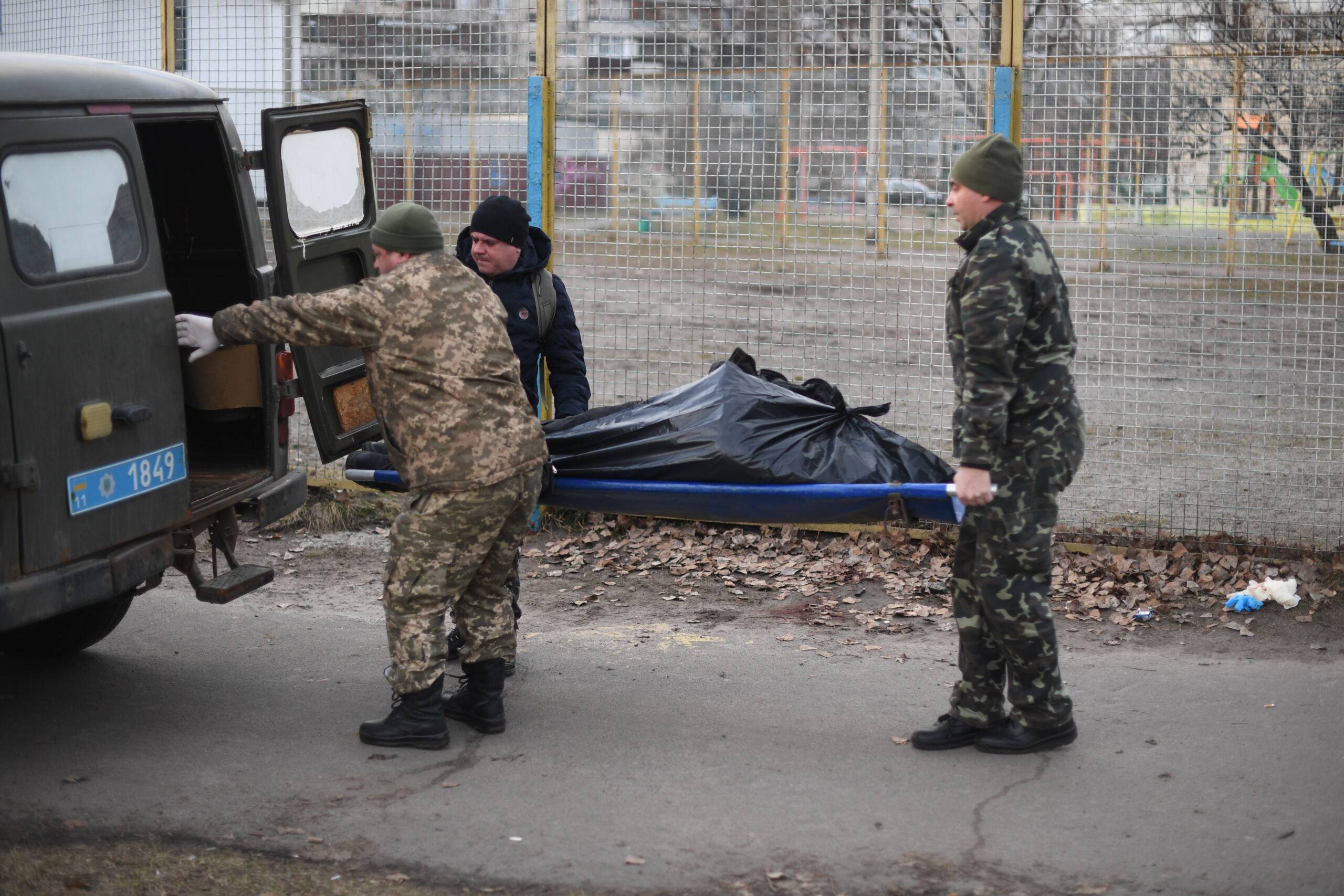 EDITORS NOTE: Graphic content / Ukrainian servicemen pick up the body of an Ukrainian man who was shot when a Russian armoured vehicle drove past him, on a sidewalk in the north of Kyiv on February 25, 2022. - Russian forces reached the outskirts of Kyiv on February 25, as Ukrainian President said the invading troops were targeting civilians and explosions could be heard in the besieged capital. (Photo by Daniel LEAL / AFP)