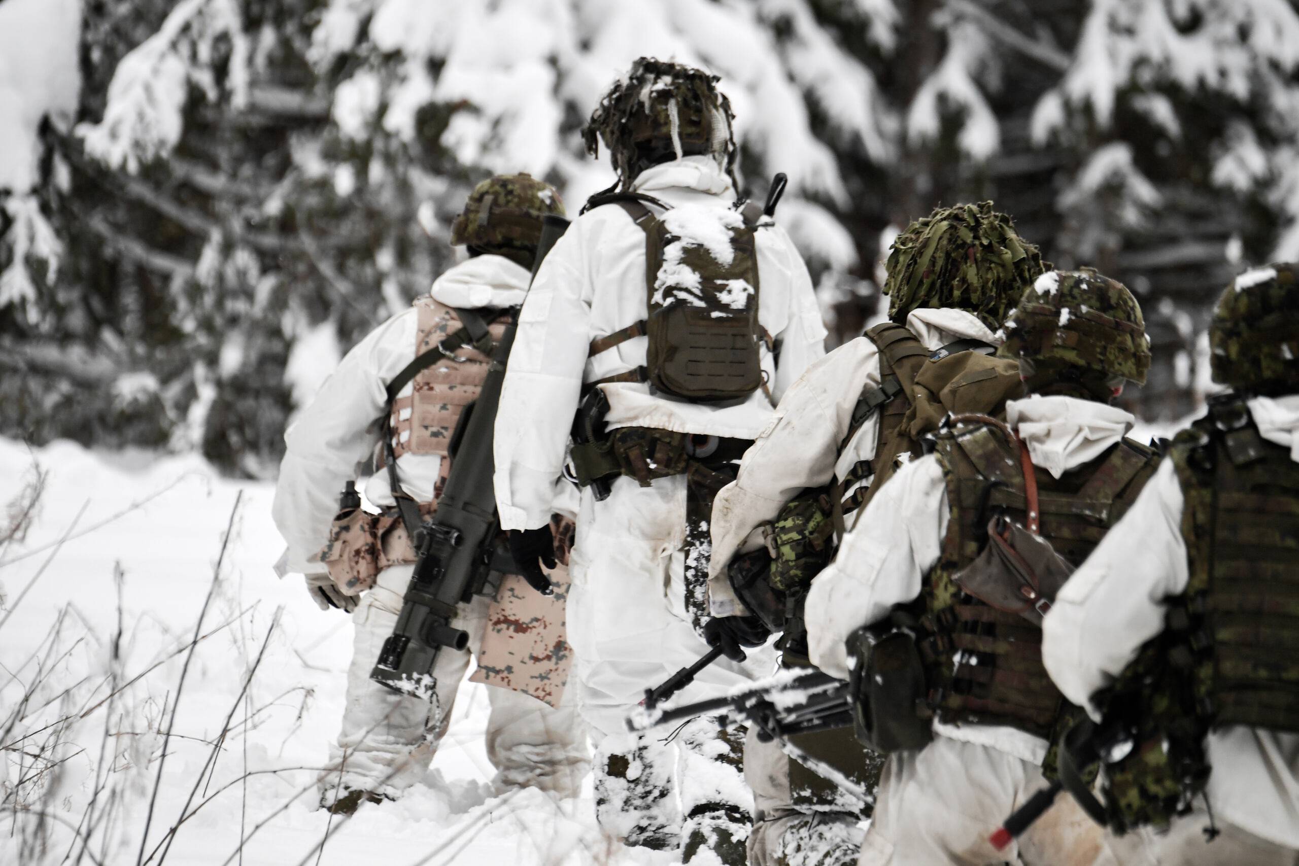 Żołnierze w maskujących strojach idą przez zimowy las