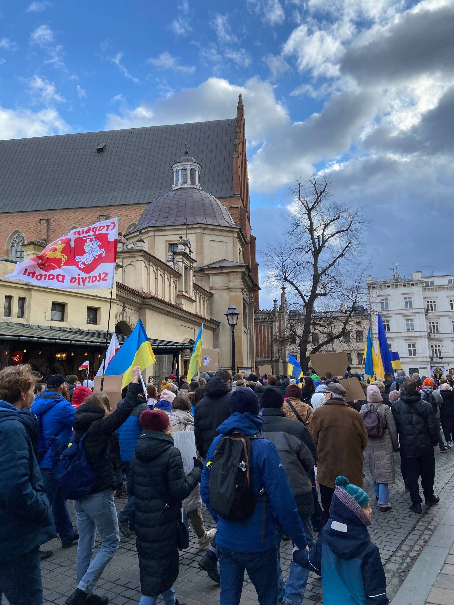 Ludzie idą ulica Stolarską w Krakowie. Niosą żółto-błekitne, ukraińskie flagi