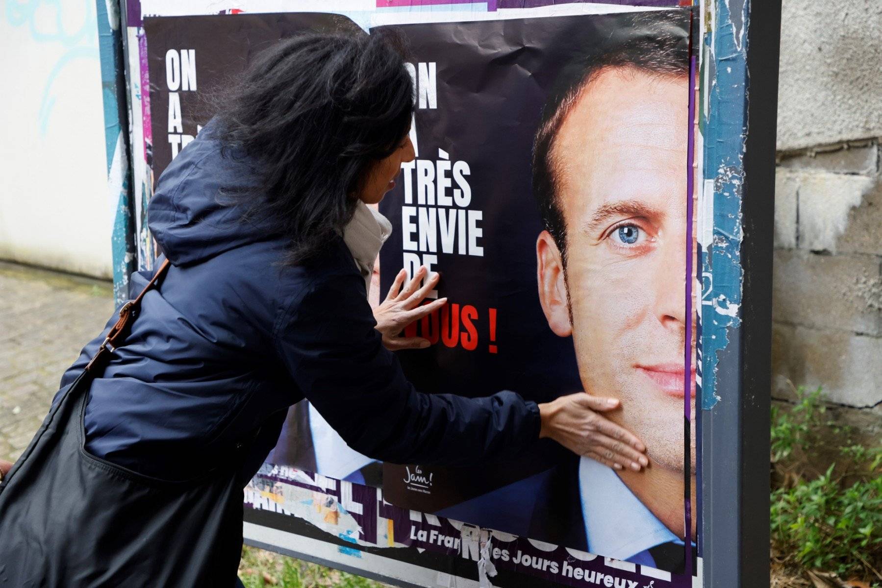 Kobieta przykeja do tablicy plakat wyborczy Macrona