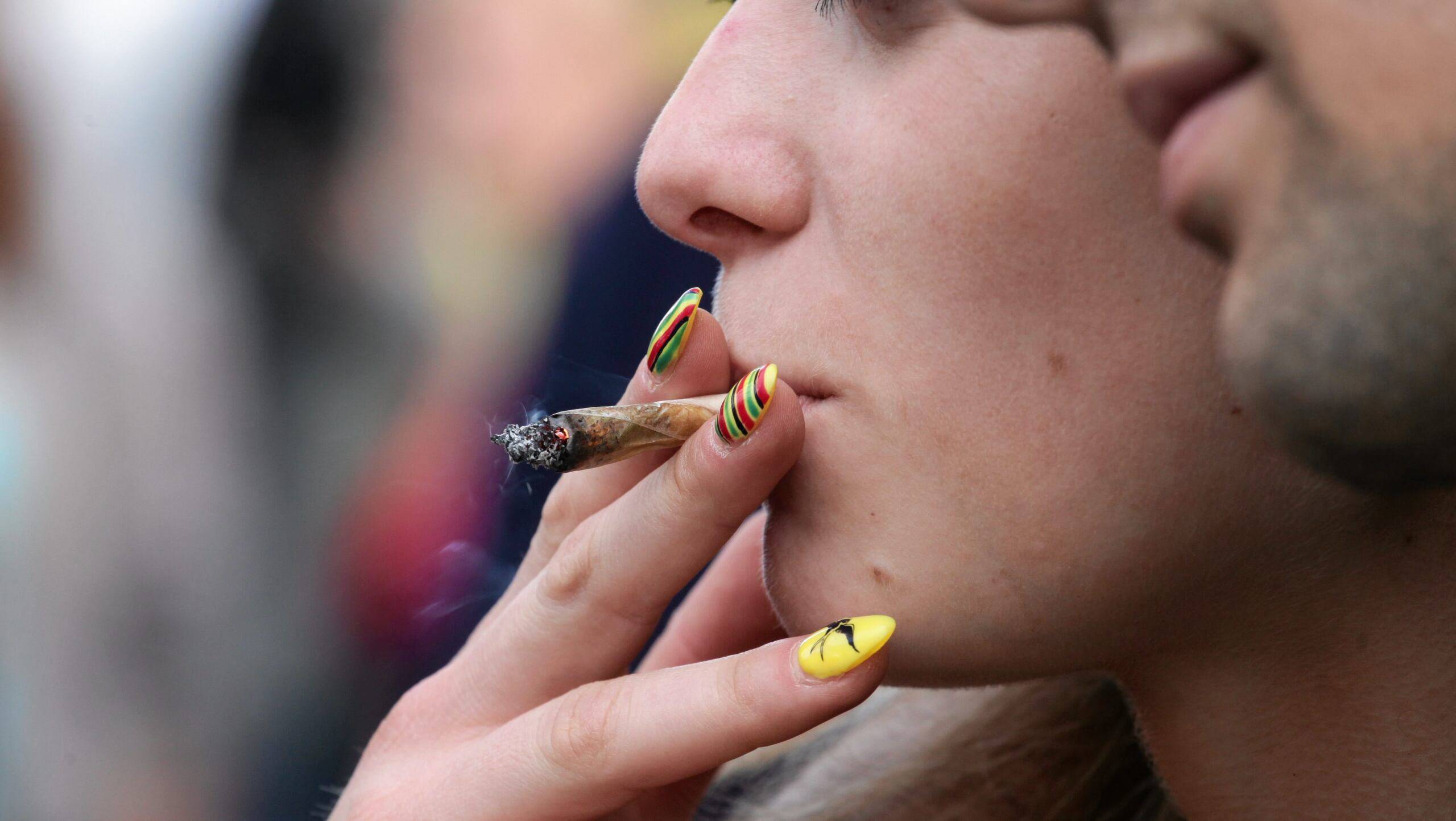 Skręt z marihuaną trzymany w ustach przez młodą kobietę z pomalowanymi paznokciami