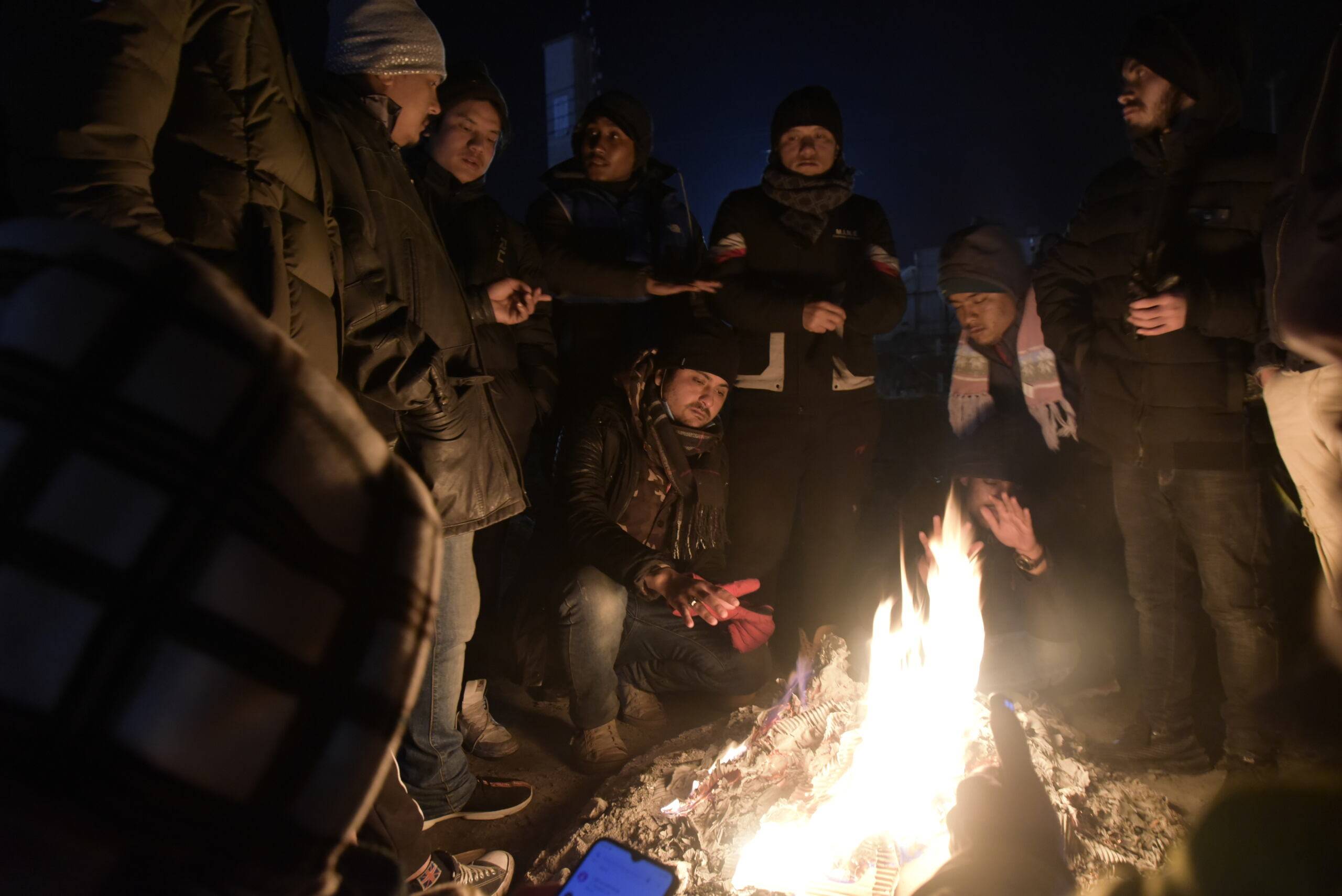 grupa uchodźców siedzi wokół ogniska w Medyce