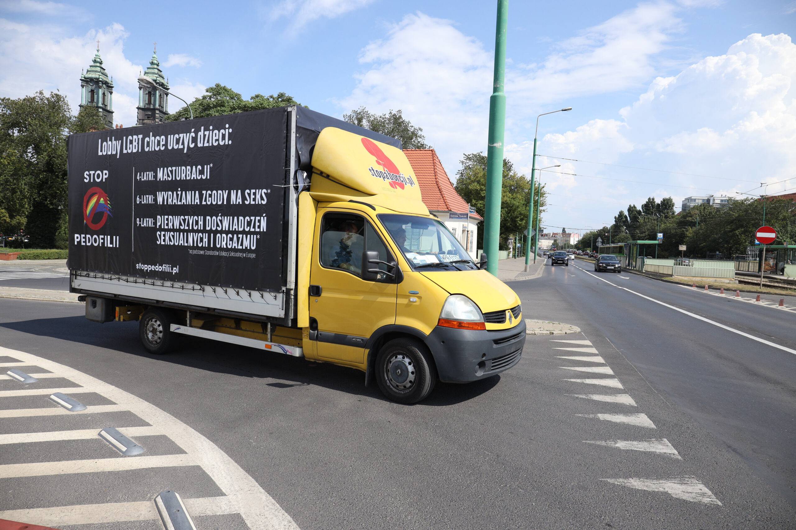 Żółty furgon dostawczy - na czarnej plandece namalowane białą farbą homobiczne hasła