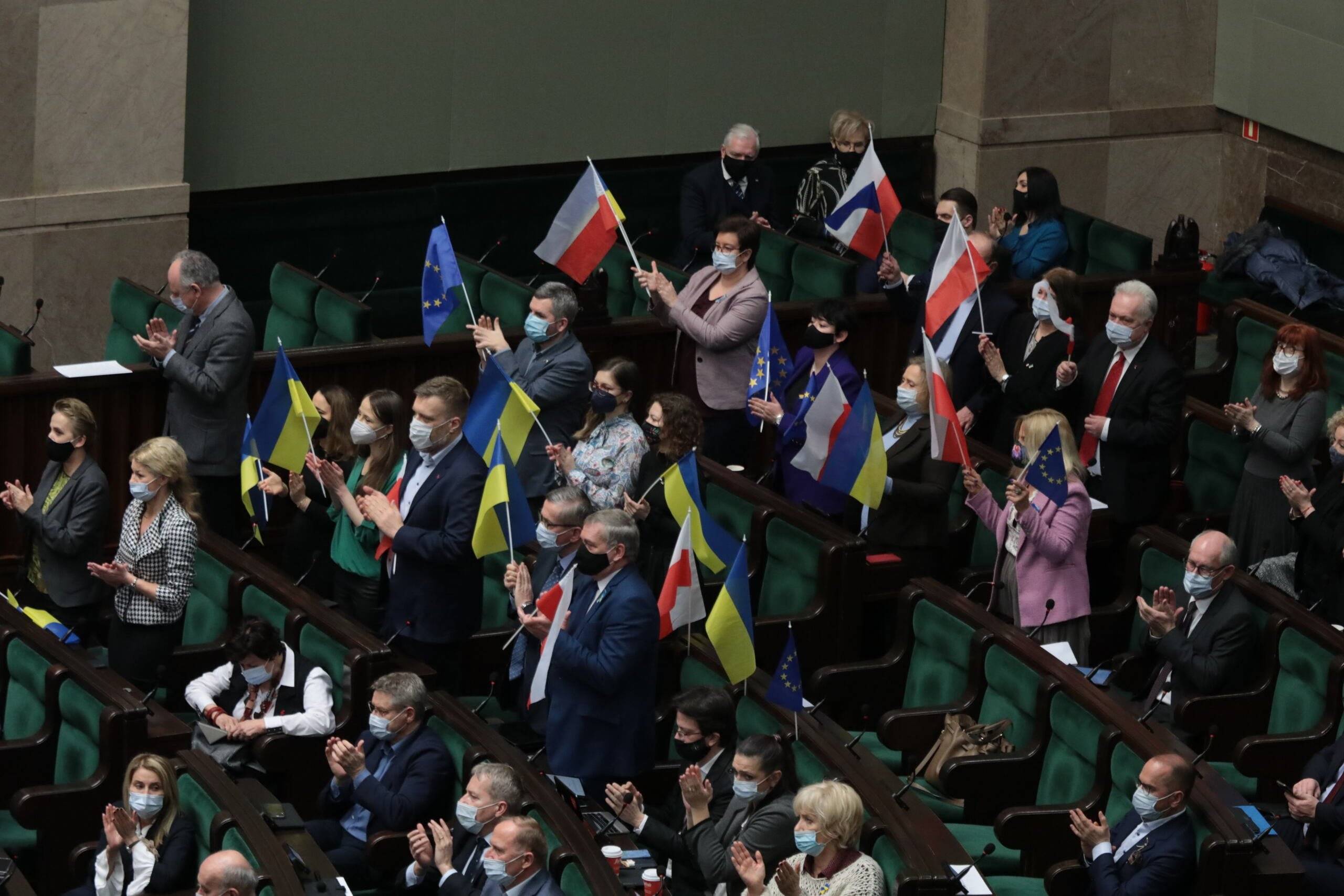 posłowie na sali plenarnej Sejmu stoją z polskimi i ukraińskimi flagami
