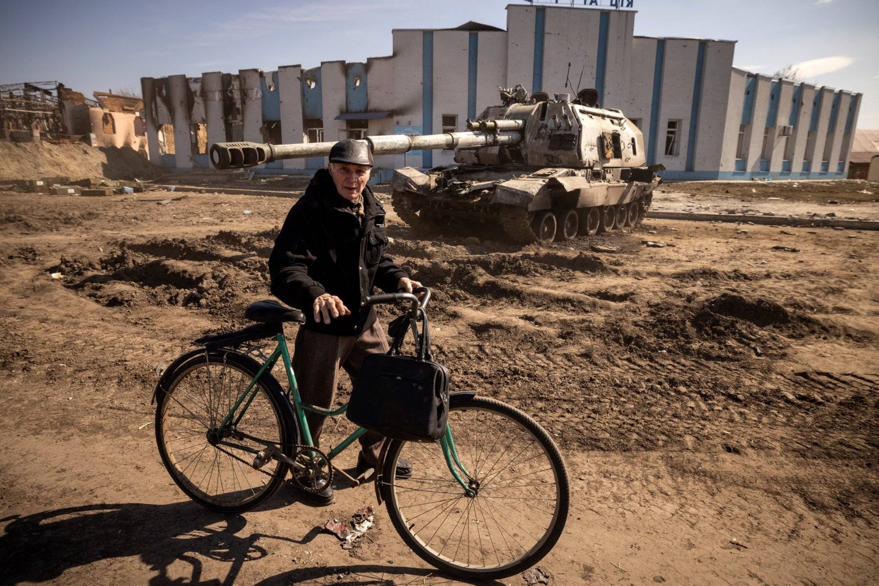Mężczyzna prowadzi rower obok zniszczonego czołgu rosyjskiego