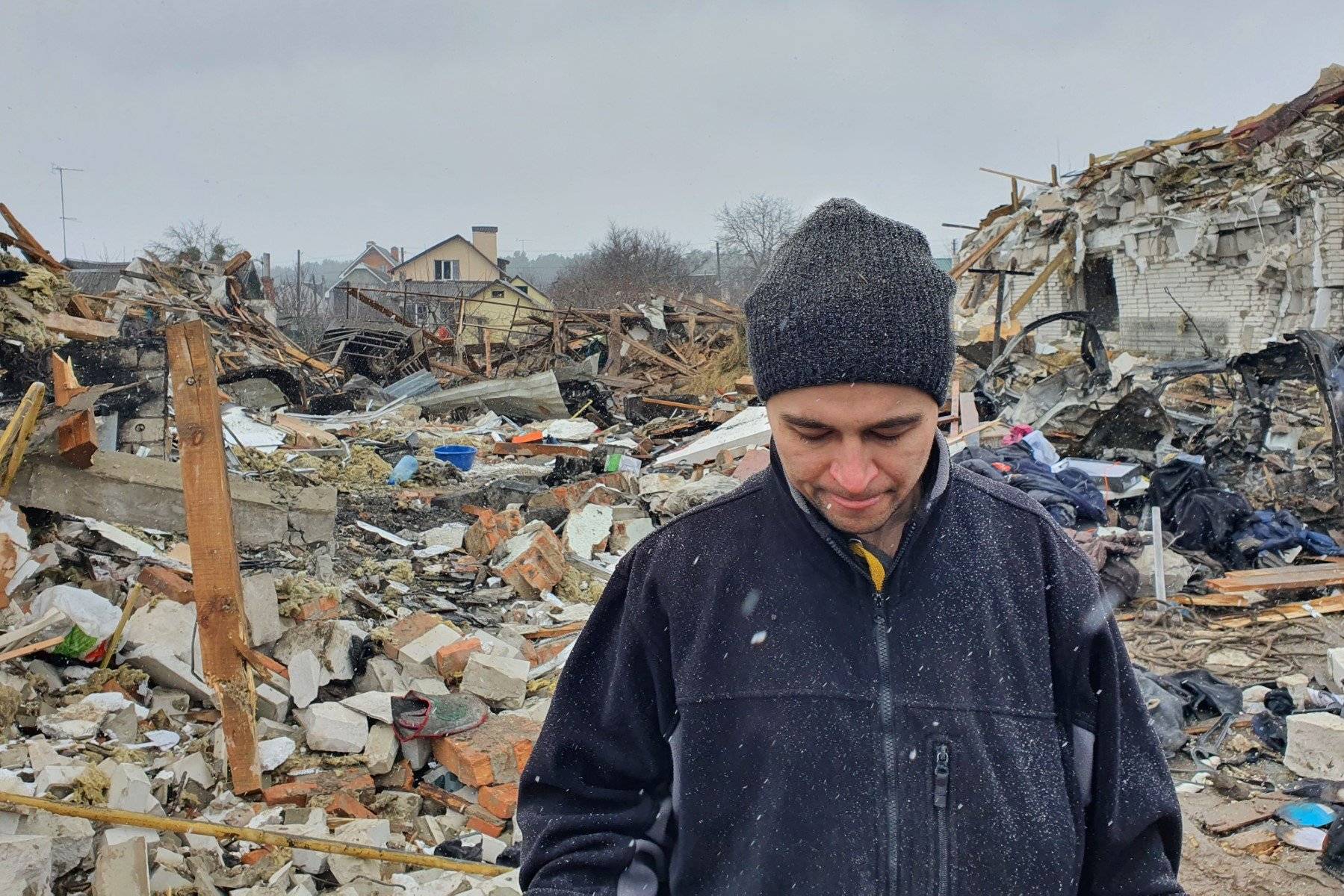 Mężczyzna z opuszczoną głową na tle gruzów swego zbombardowanego domu