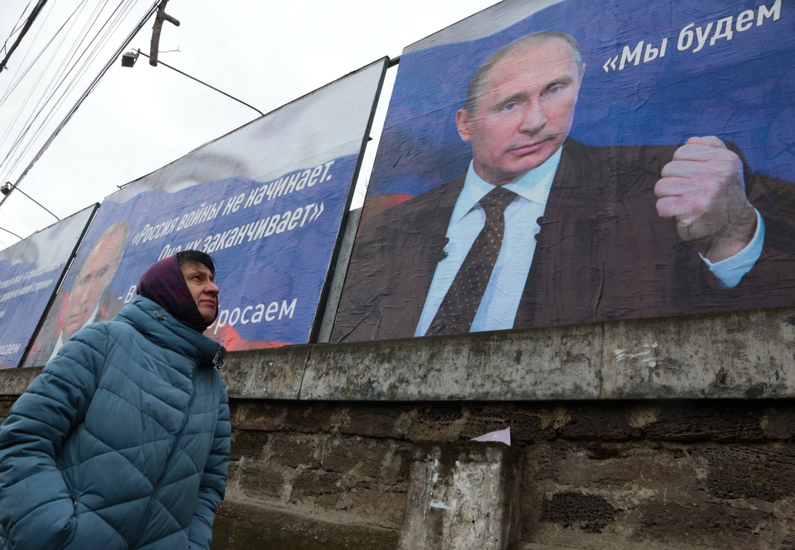 Kobieta przechodzi obok ogromnych plakatów z wizerunkami prezydenta Rosji Władimira Putina i czyta „Rosja nie zaczyna wojen, ona je kończy” (L) i „Będziemy dążyć do demilitaryzacji i denazyfikacji Ukrainy” w centrum Symferopola na Krymie , 4 marca 2022 r.