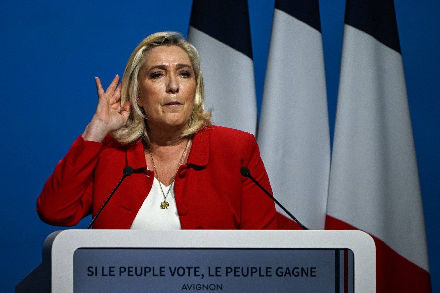 Kobieta, blondynka, w czerwonej marynarce na scenie nadstawia ucha by usłyszeć pytanie z sali. Marine Le Pen