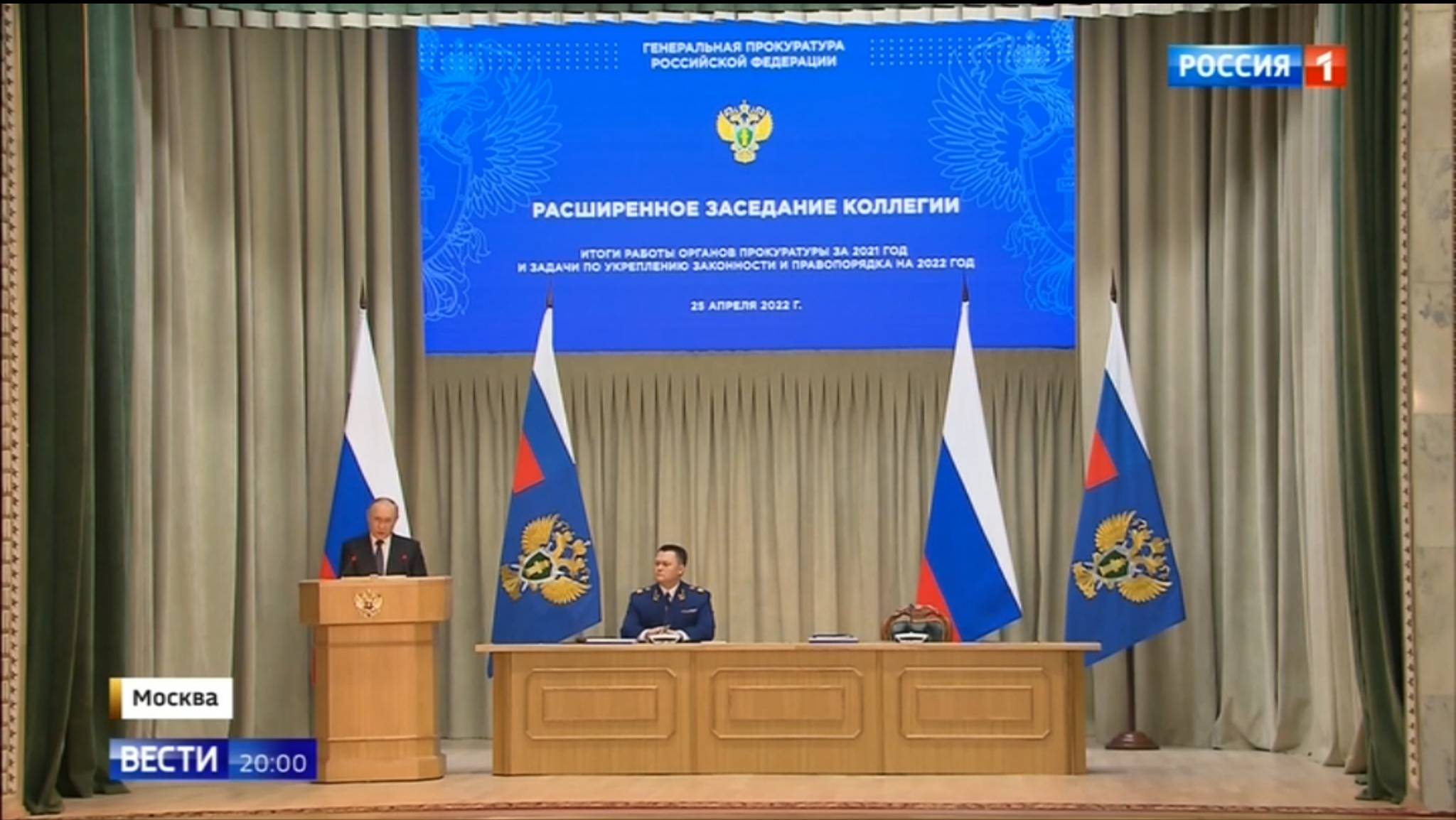 Męzczyzna na mównicy (Putin), pozostali - w prezydium, z tyłu rosyjskie flagi
