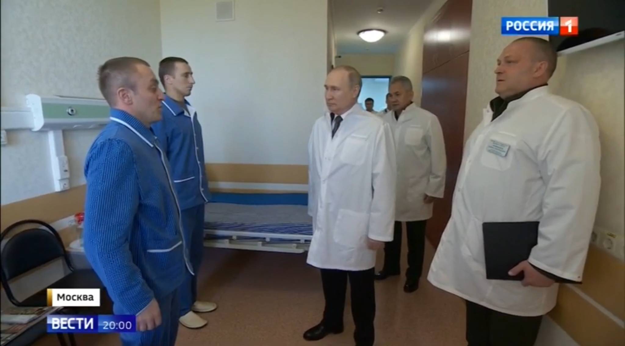 Mężczyźni w piżamach na stojąco rozmawiają z Putinem w białym fartuchu