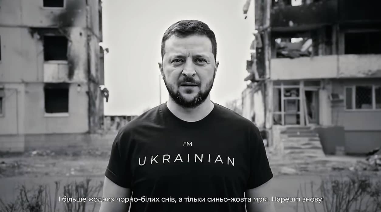 Prezydentr Zełenski z koszulce z napisem Im Ukrainian na tle zburzonego domu mieszkalnego