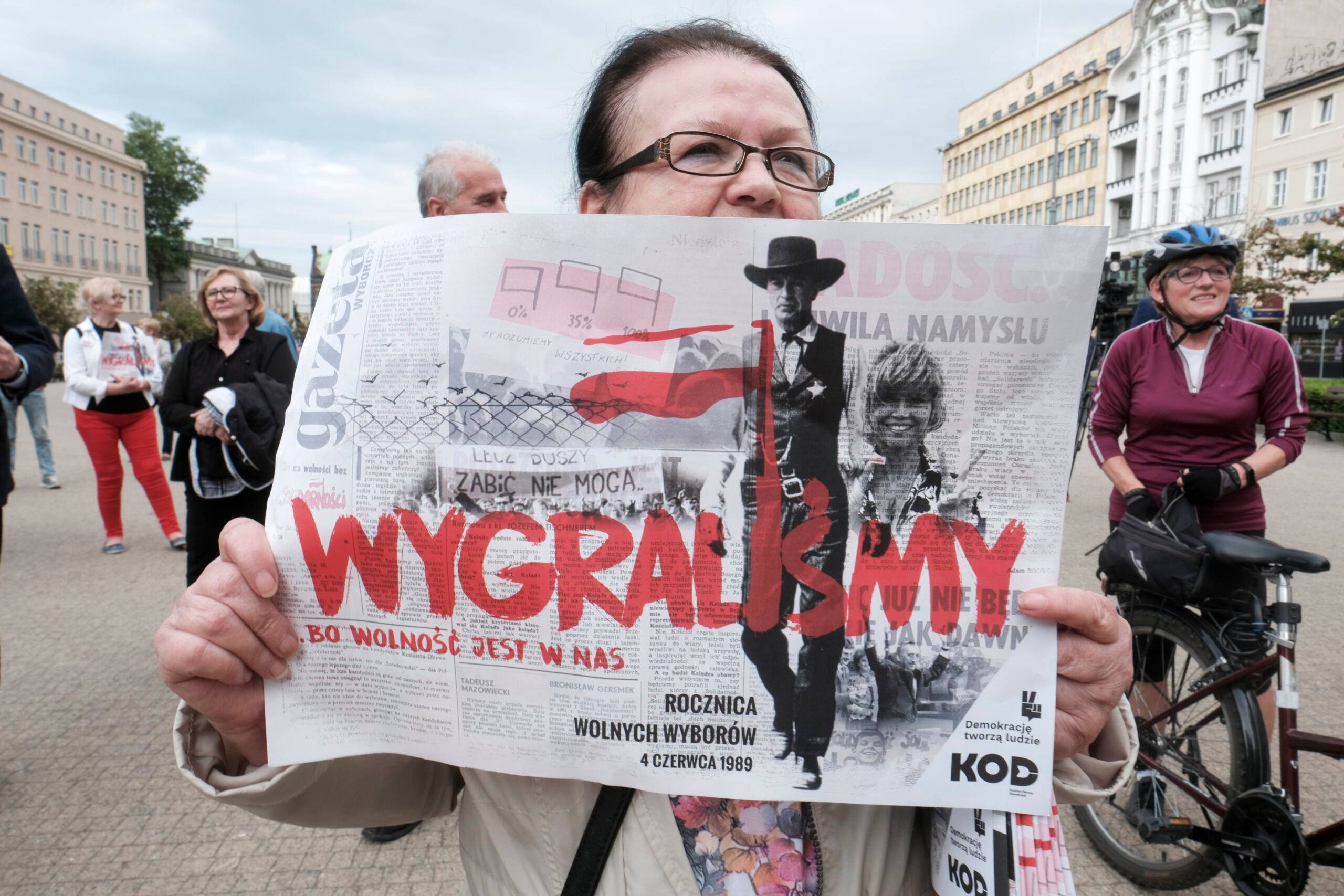 Kobieta z plakatem z napisem Wygraliśmy na tle plakatu wyborczego S z 1989 r