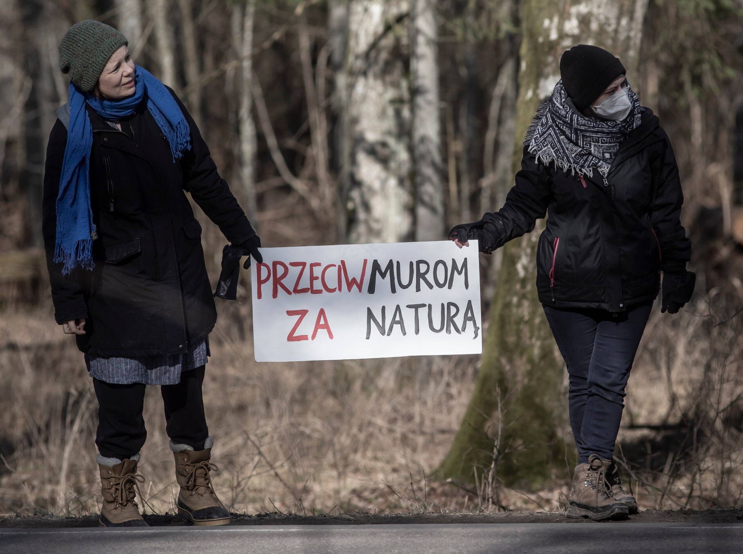 kobiety w lesie trzymające transparenty przeciw murowi na granicy polsko-białoruskiej