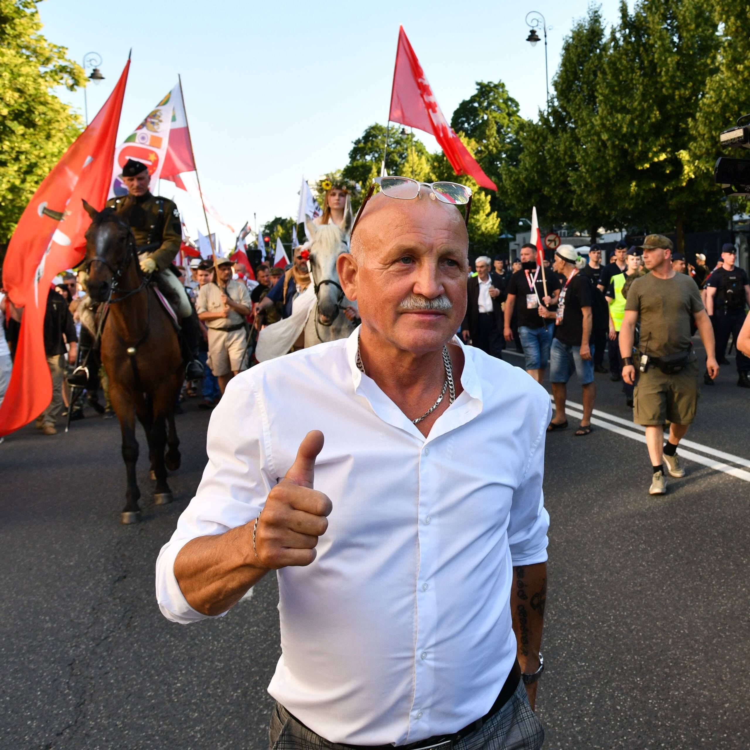 Mężczyna w białek koszuli idzie środkiem ulicy, srebrny łańcuch na szyi, Piotr Rybak