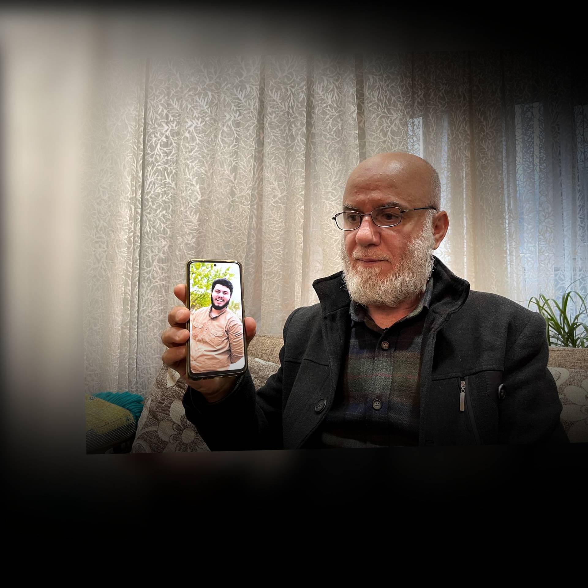 Ojciec (mężczyzna z siwą brodą) pokazuje na telefonie komórkowym zdjęcie syna