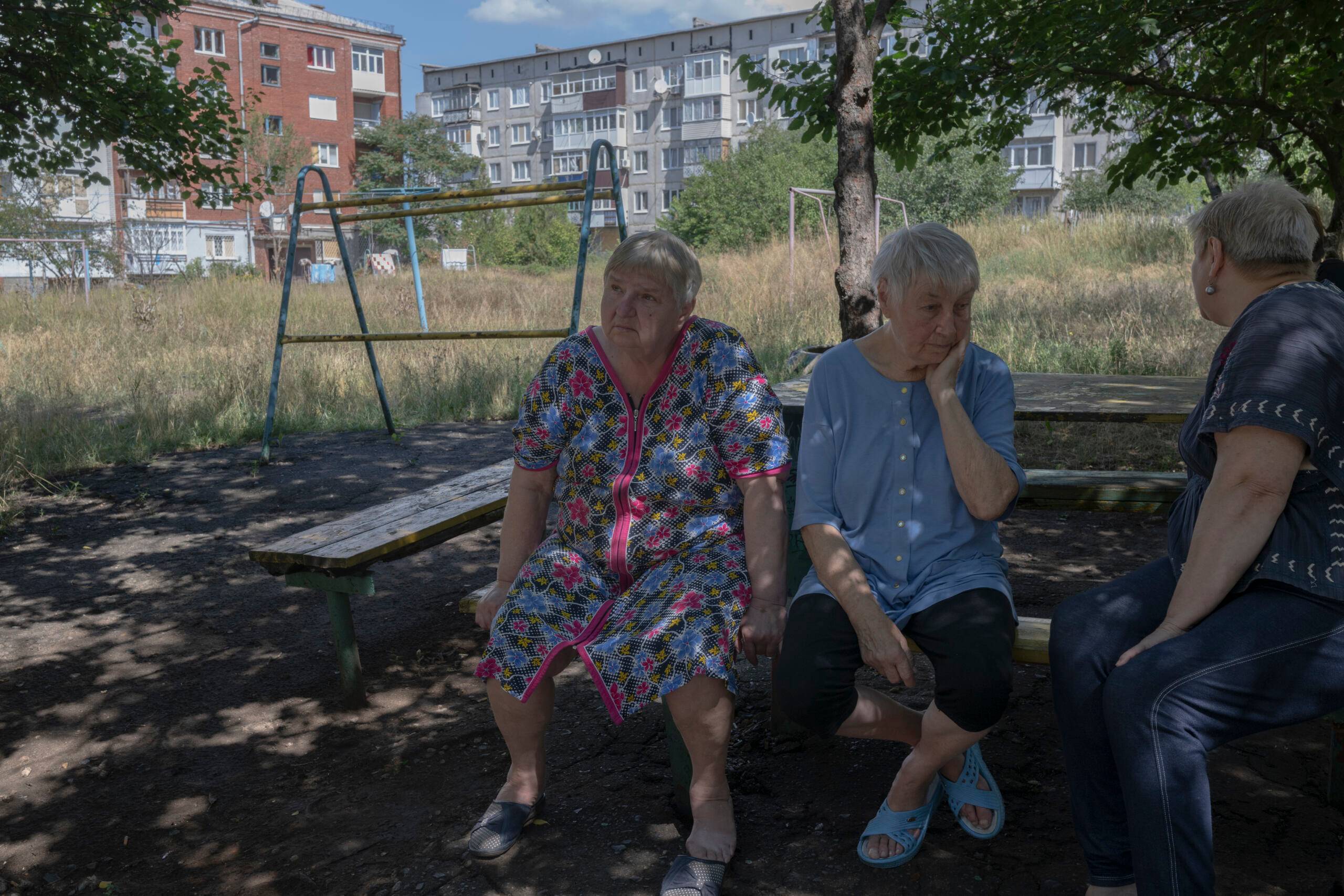 Trzy starsze kobiety siedzą na ławce przy zarośniętym placu zabaw