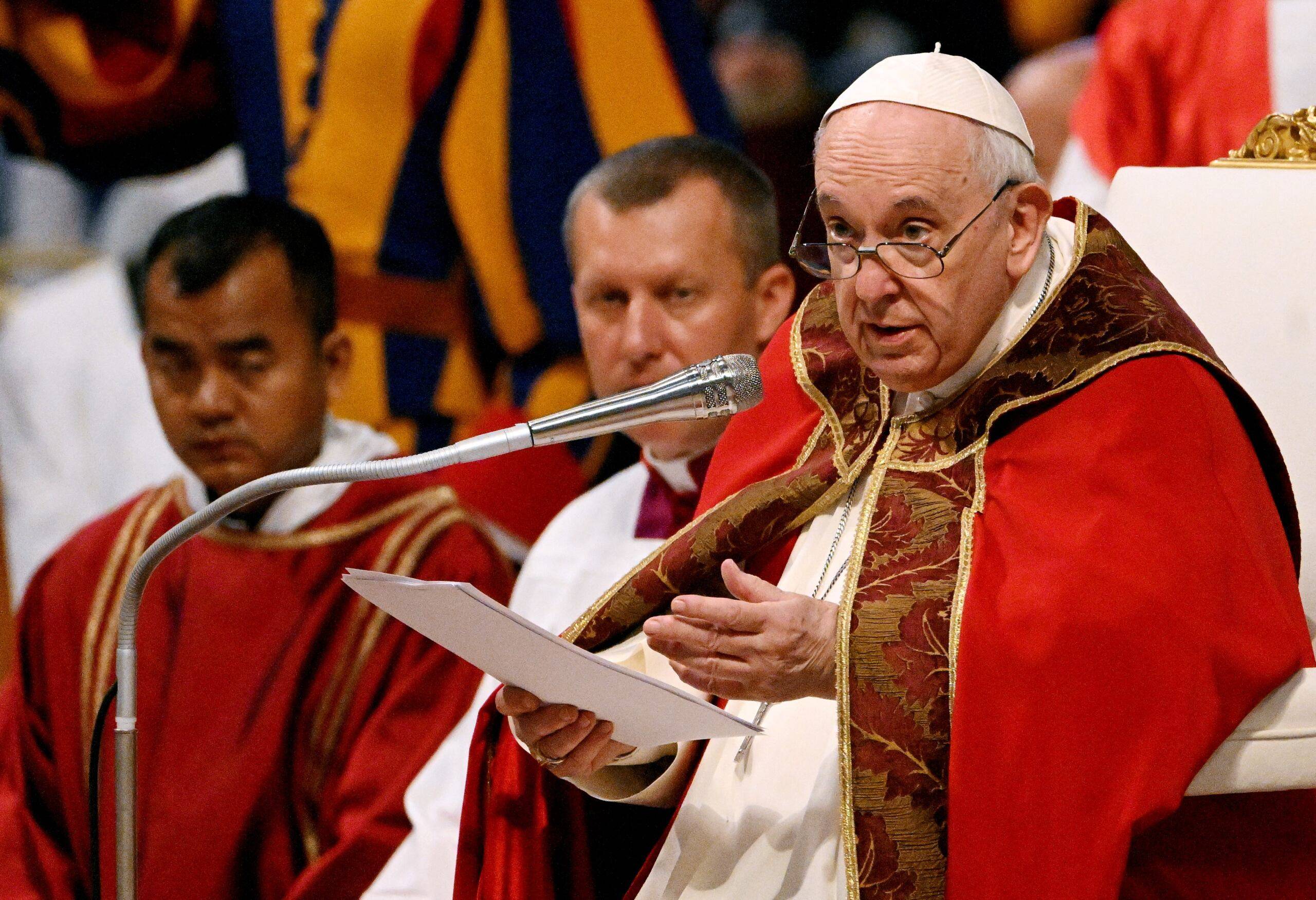 Papież Franciszek w czerwnym odzieniu w okulrach wygłąsza kazanie, przed nim mikrofon
