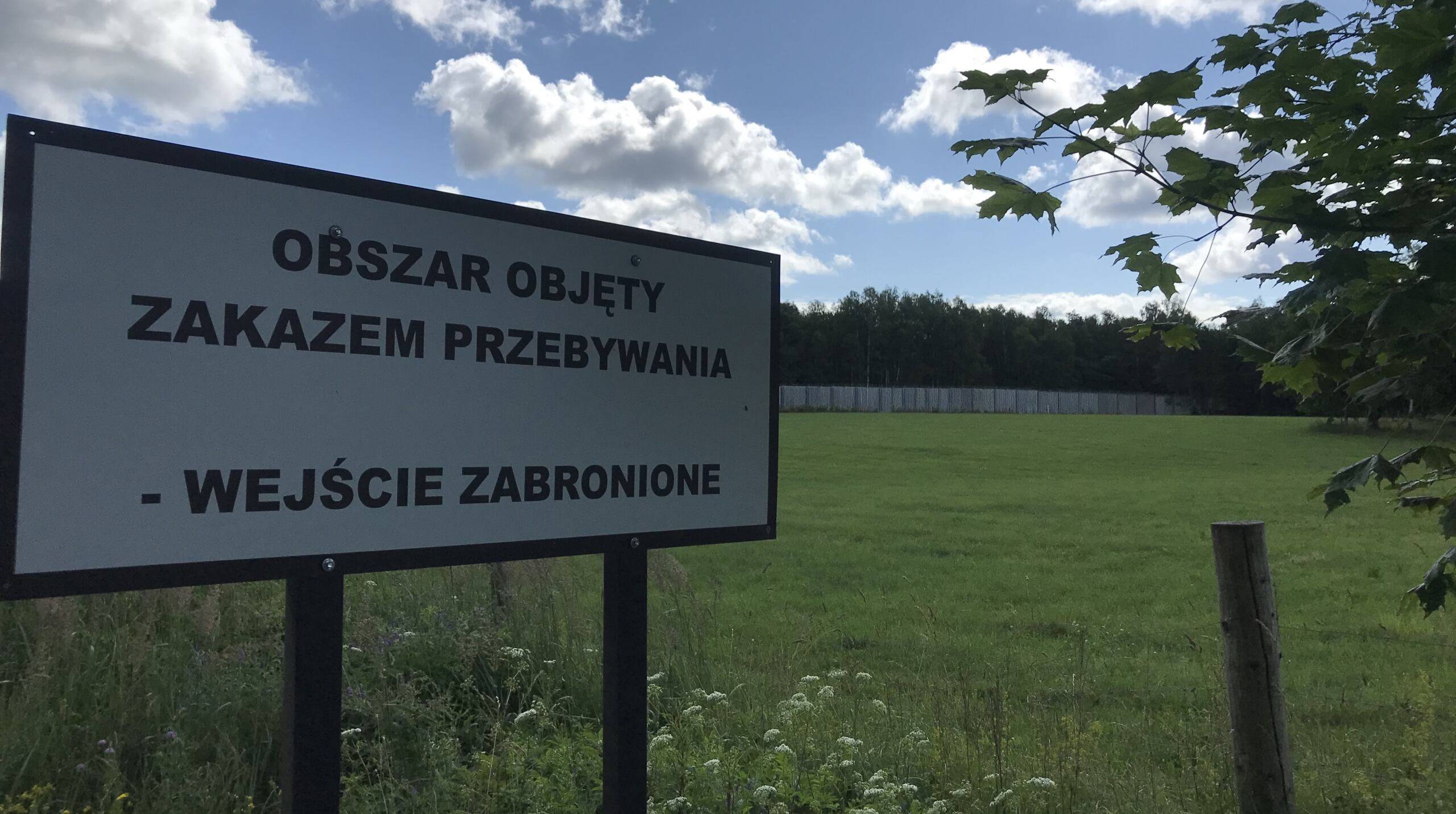 Tablica informująca o zakazie przebywania, w tle mur graniczny