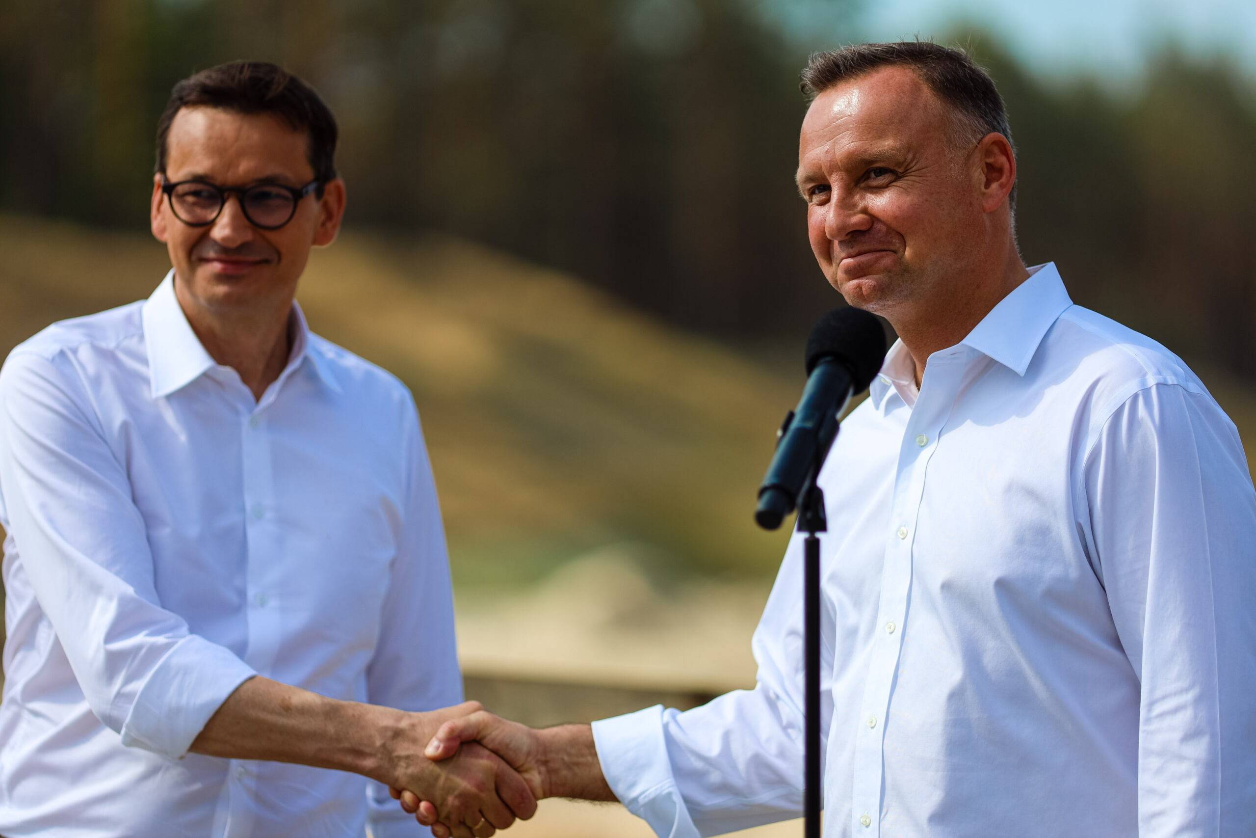 Mateusz Morawiecki i Andrzej Duda podają sobie ręce, ubrani w białe koszule z podwiniętymi rękawami