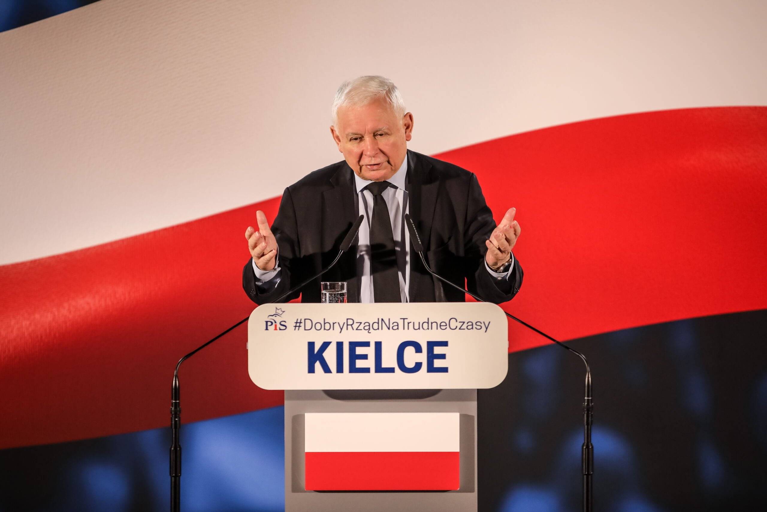 Jarosław Kaczyński przemawia na tle biało-czerwonej flagi