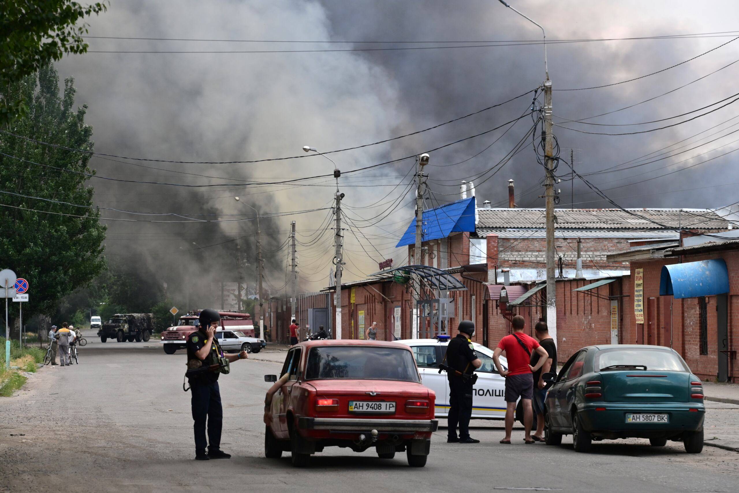 Pracownicy ochrony zatrzymują kierowców, gdy dym unosi się z centralnego rynku w Słowiańsku, na północ od Kramatorska, 5 lipca 2022 roku, po podejrzanym ataku rakietowym w trakcie rosyjskiej inwazji na Ukrainę.