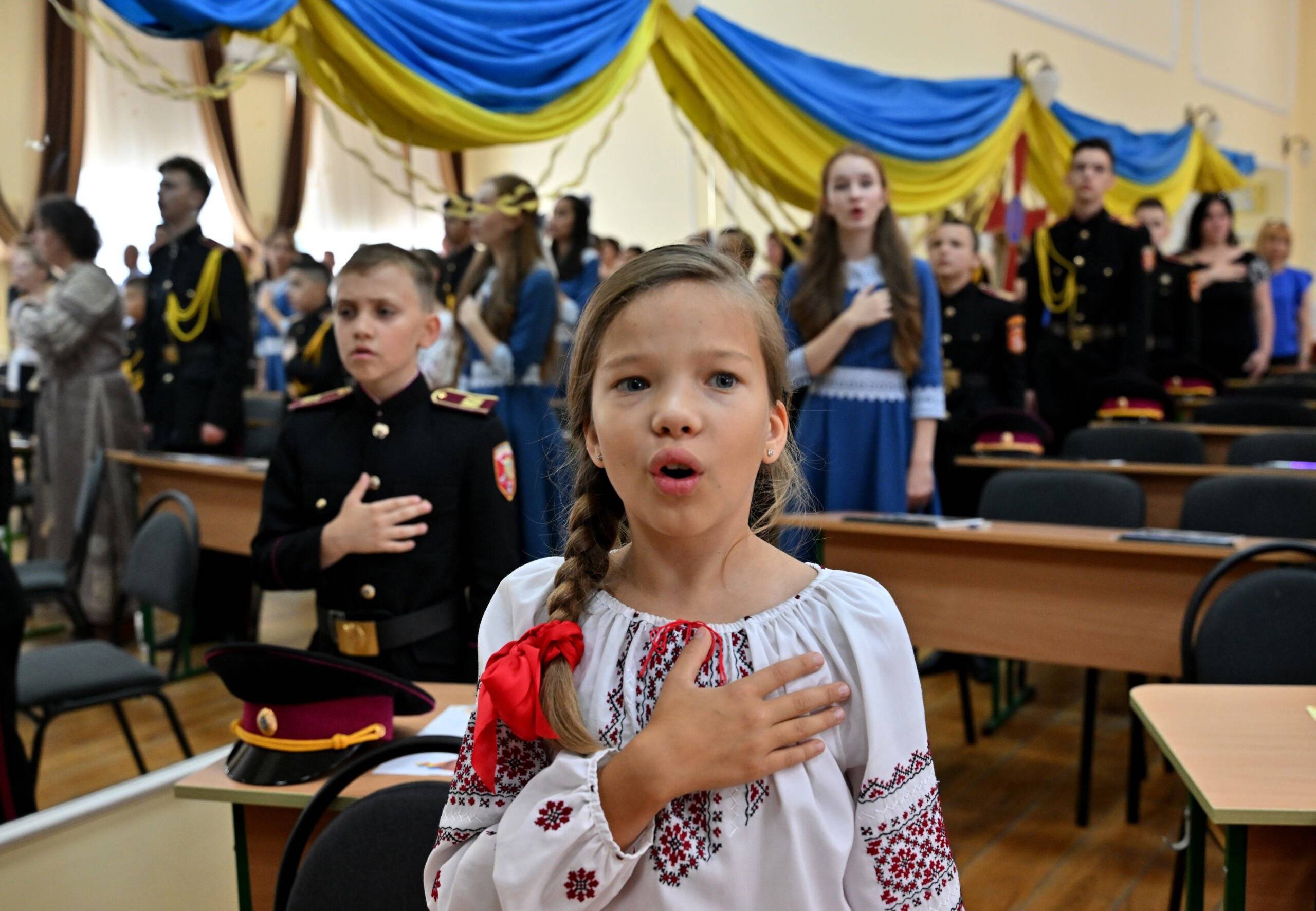Dziewczynka z ręką na sercu śpiewa hymn w ukraińskiej szkole