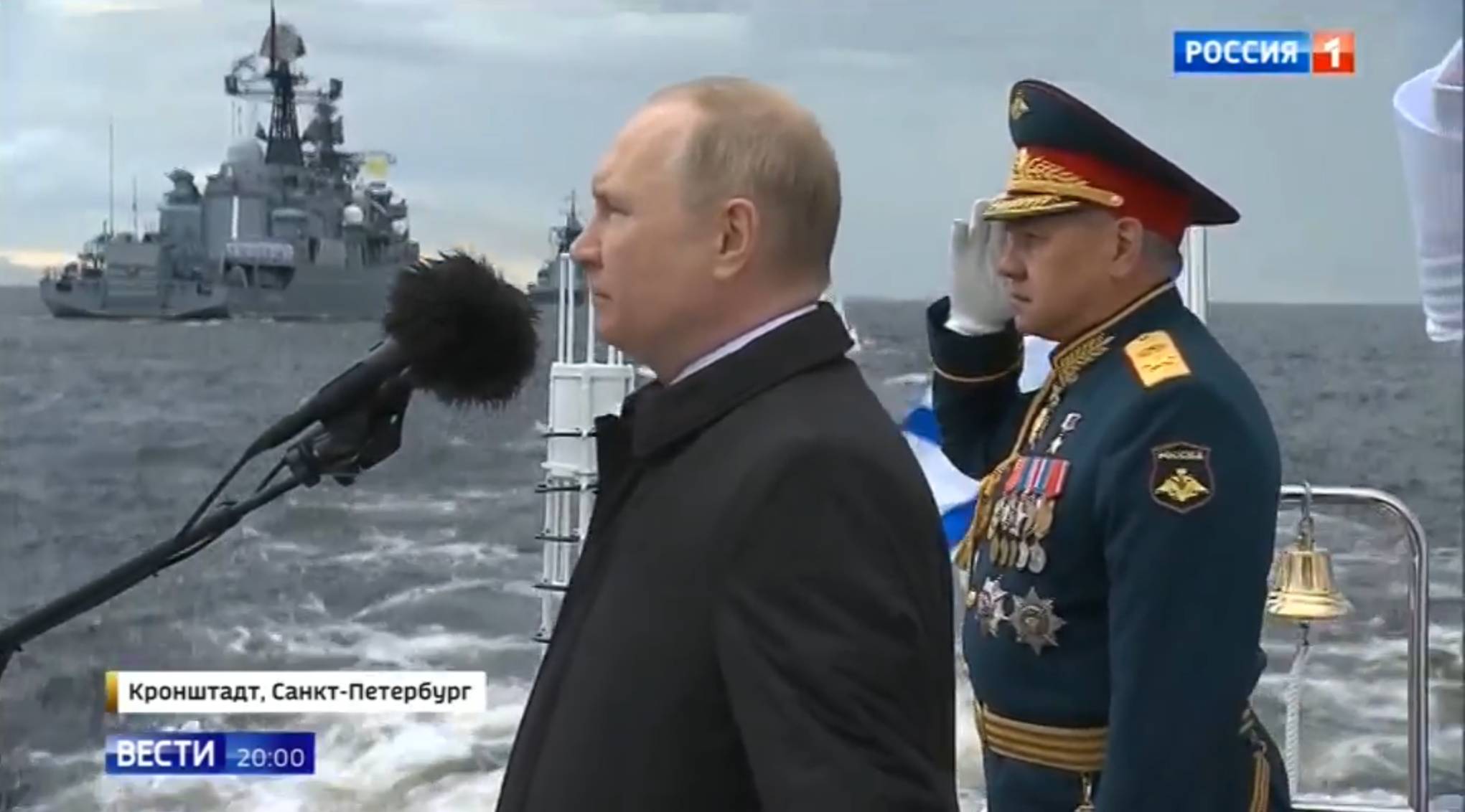 Putin mówi przez mikrofon do okrętu. Obok Szojgu w mundurze