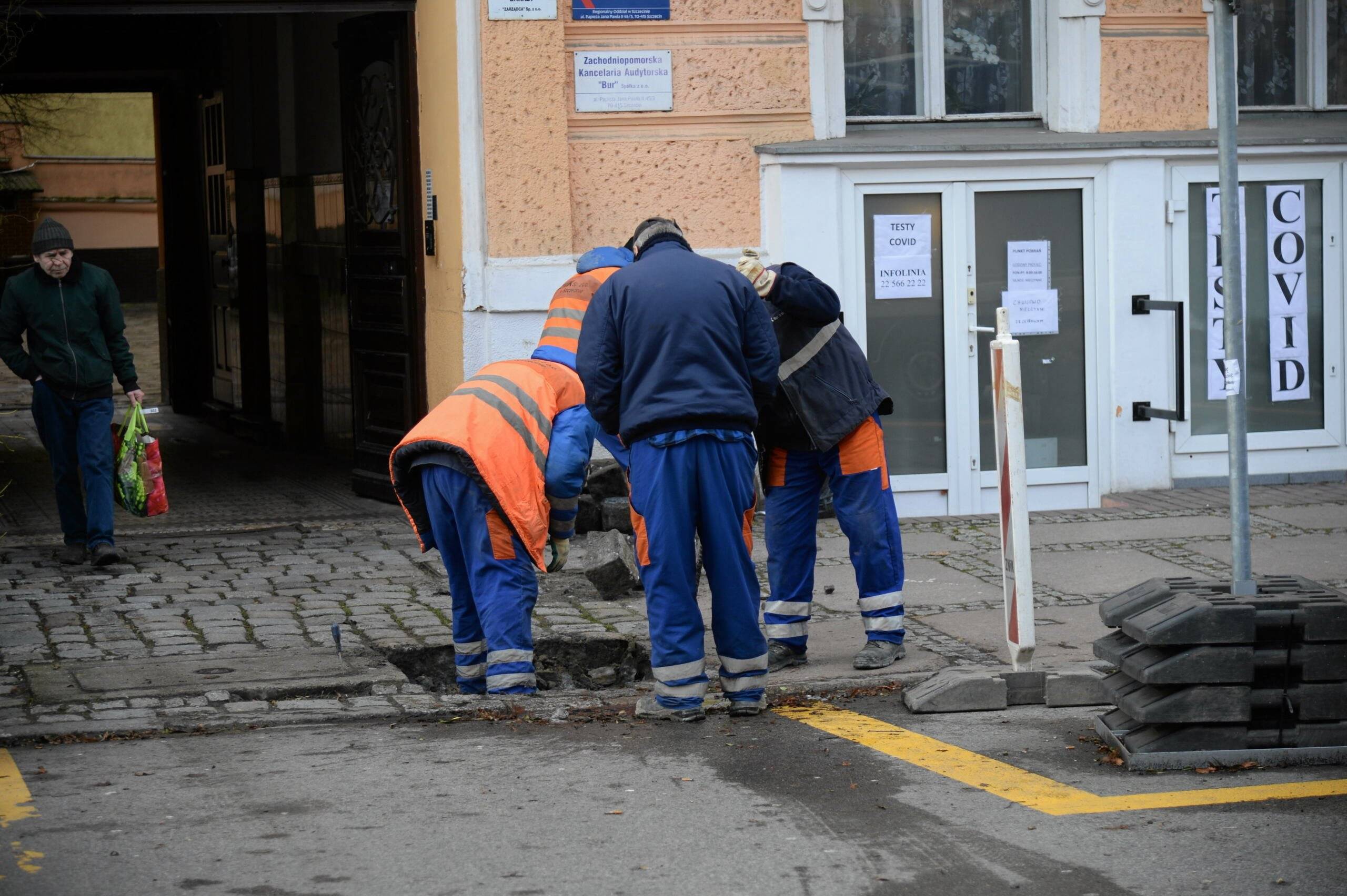 Robotnicy w ubraniach roboczych pochylają się nad dziurą w chodniku