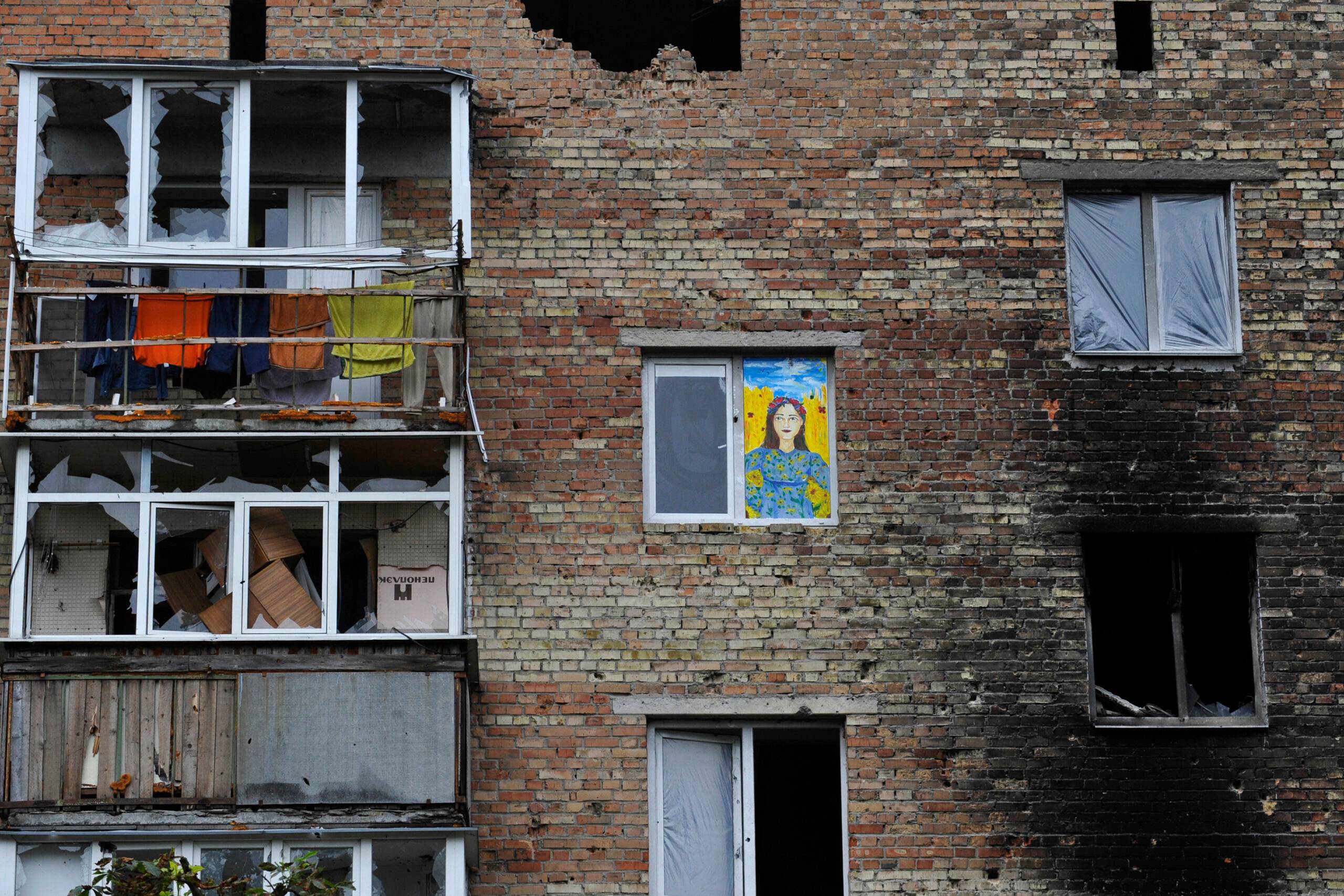 Zniszczony dom, w oknie - rysunek przedstawiający kobietę w niebieskim i żółtym kolorze (barwach Ukrainy)