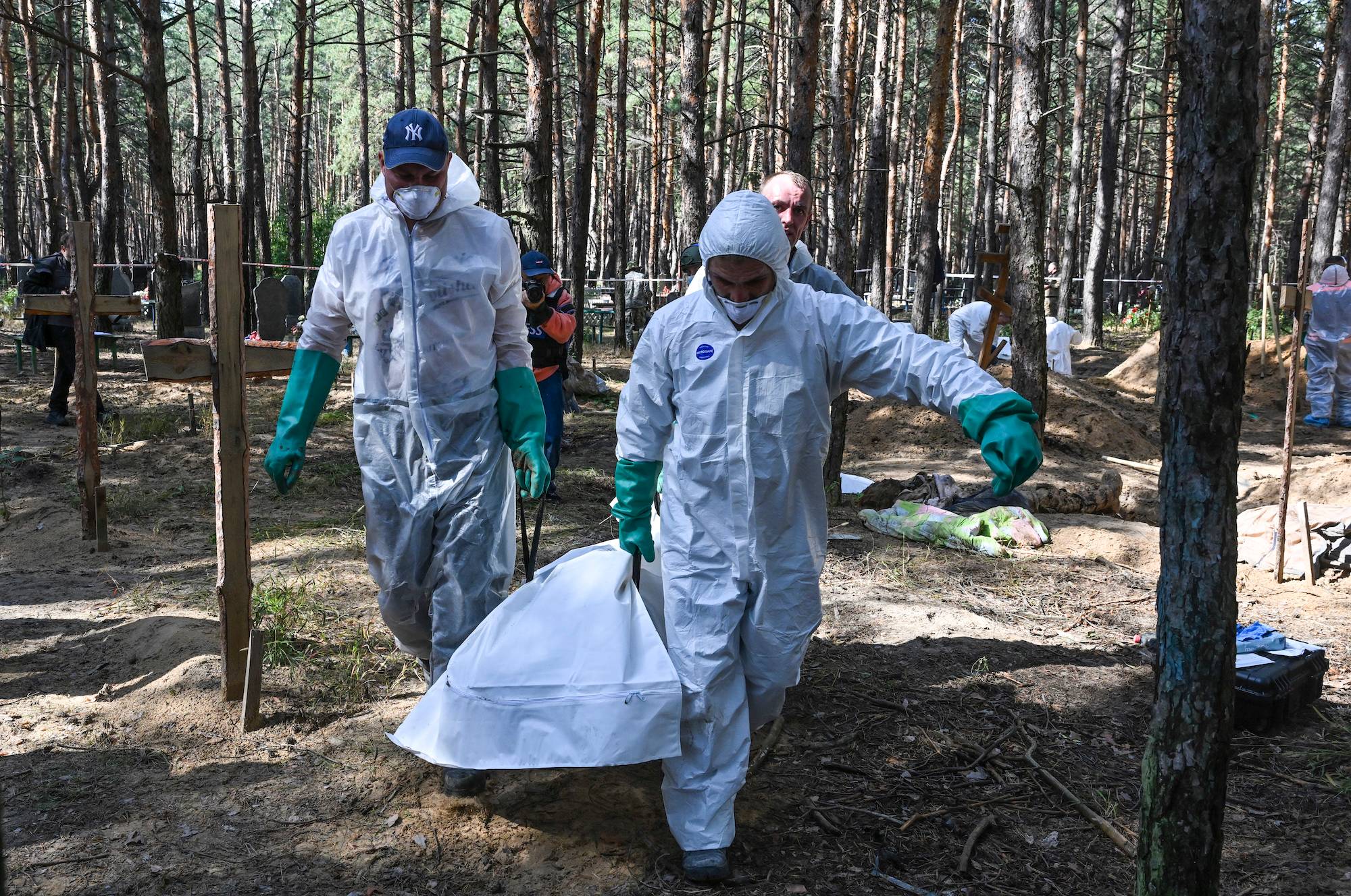 EDITORS NOTE: Graphic content / Forensic technicians carry a bodybag at the site of a mass grave in a forest on the outskirts of Izyum, eastern Ukraine on September 18, 2022. - Ukrainian authorities discovered around 450 graves outside the formerly Russian-occupied city of Izyum with some of the exhumed bodies showing signs of torture. (Photo by Juan BARRETO / AFP)