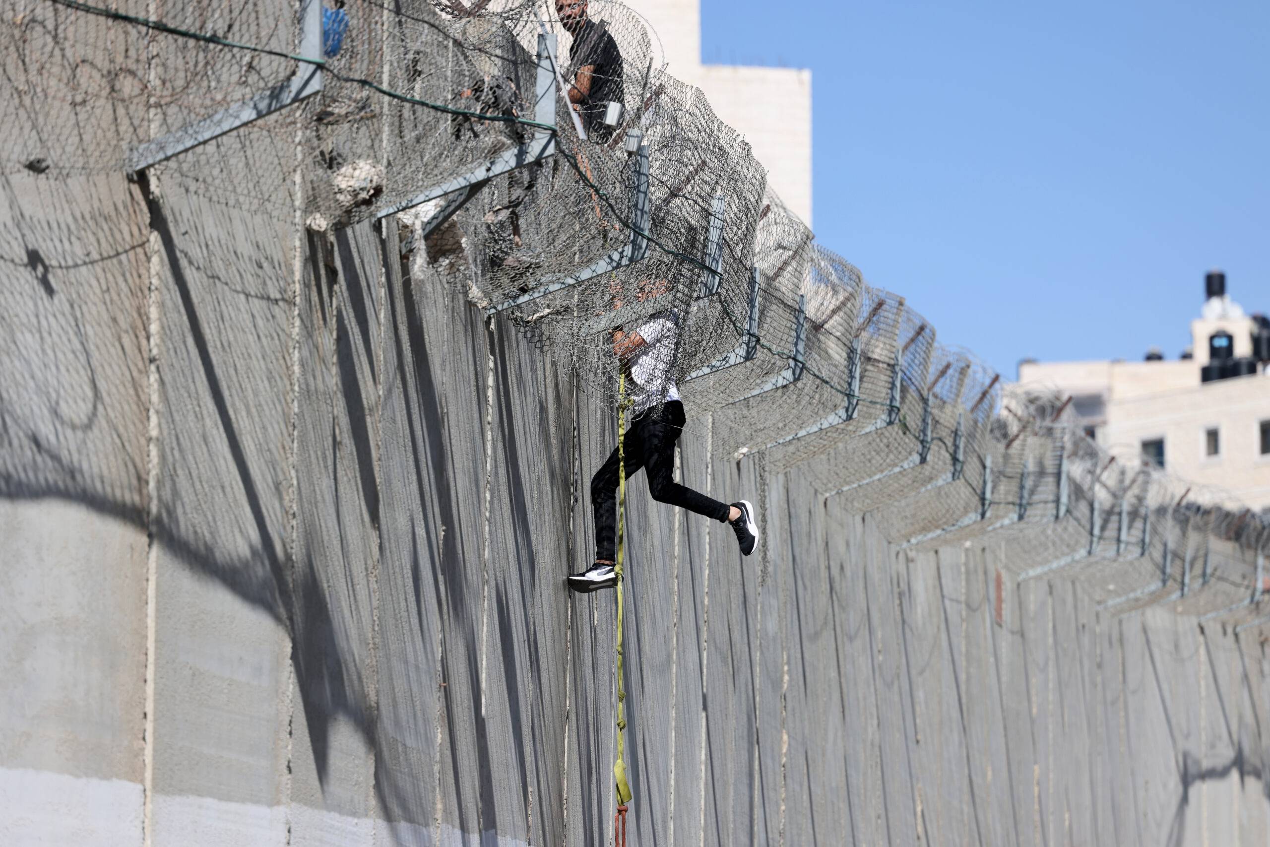 A youth descends on a rope across the concrete wall of Israel's controversial separation barrier into the East Jerusalem neighbourhood of Beit Hanina after having climbed and crossed over from the village of al-Ram, on July 11, 2022. (Photo by Ahmad GHARABLI / AFP)