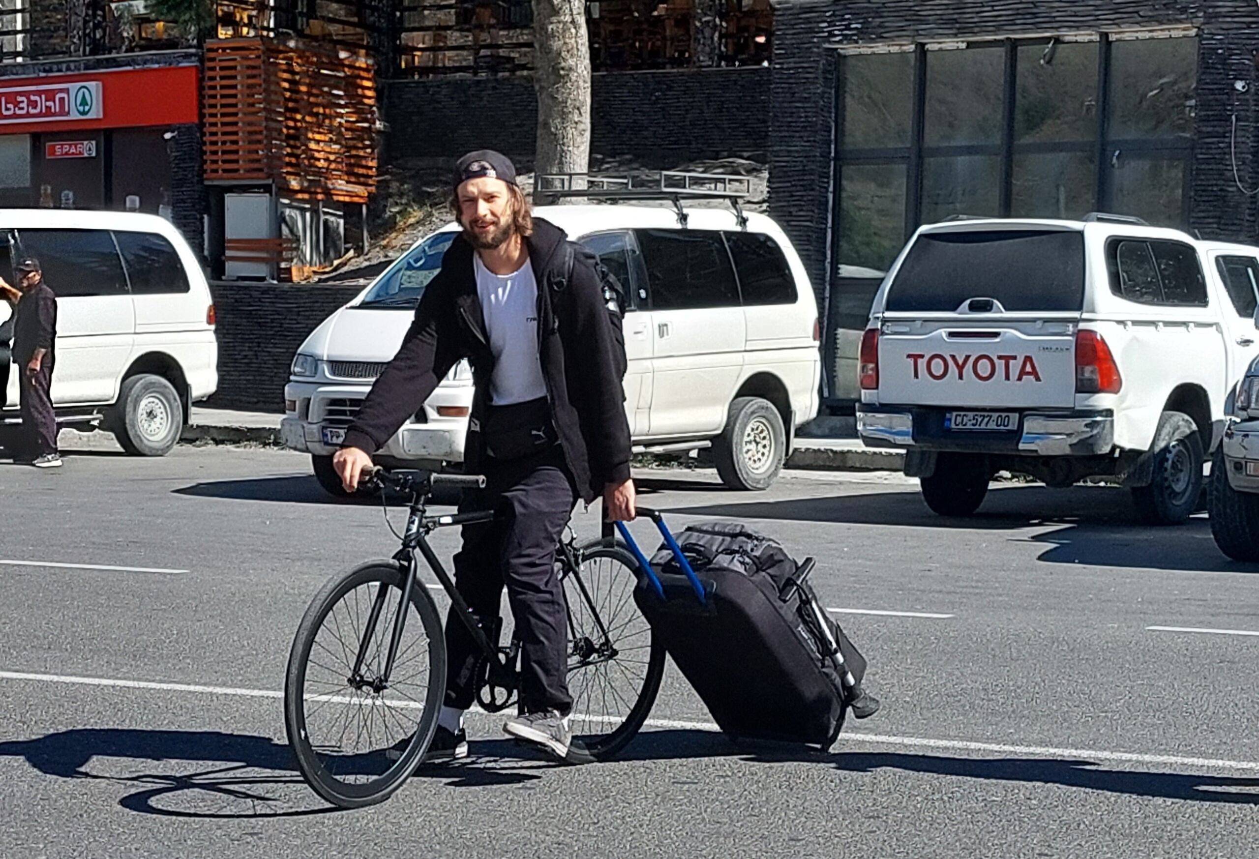 mężczyzna na rowerze ciągnie walizkę na kółkach